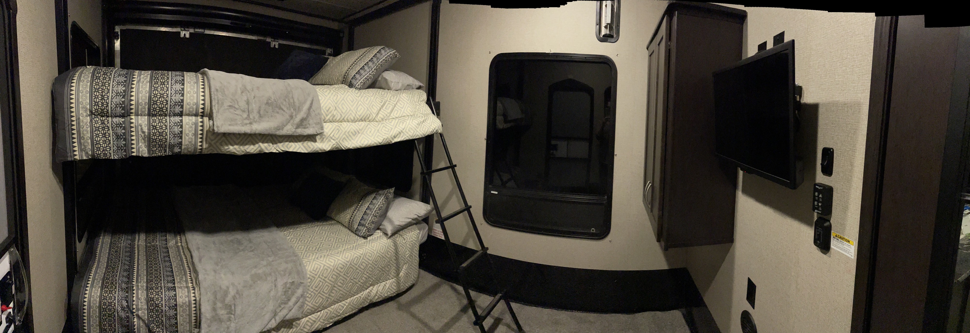 This RV rental interior showcases comfortable bunk beds with a ladder, TV, and storage cabinet, ideal for family trips.. Keystone Carbon 2017
