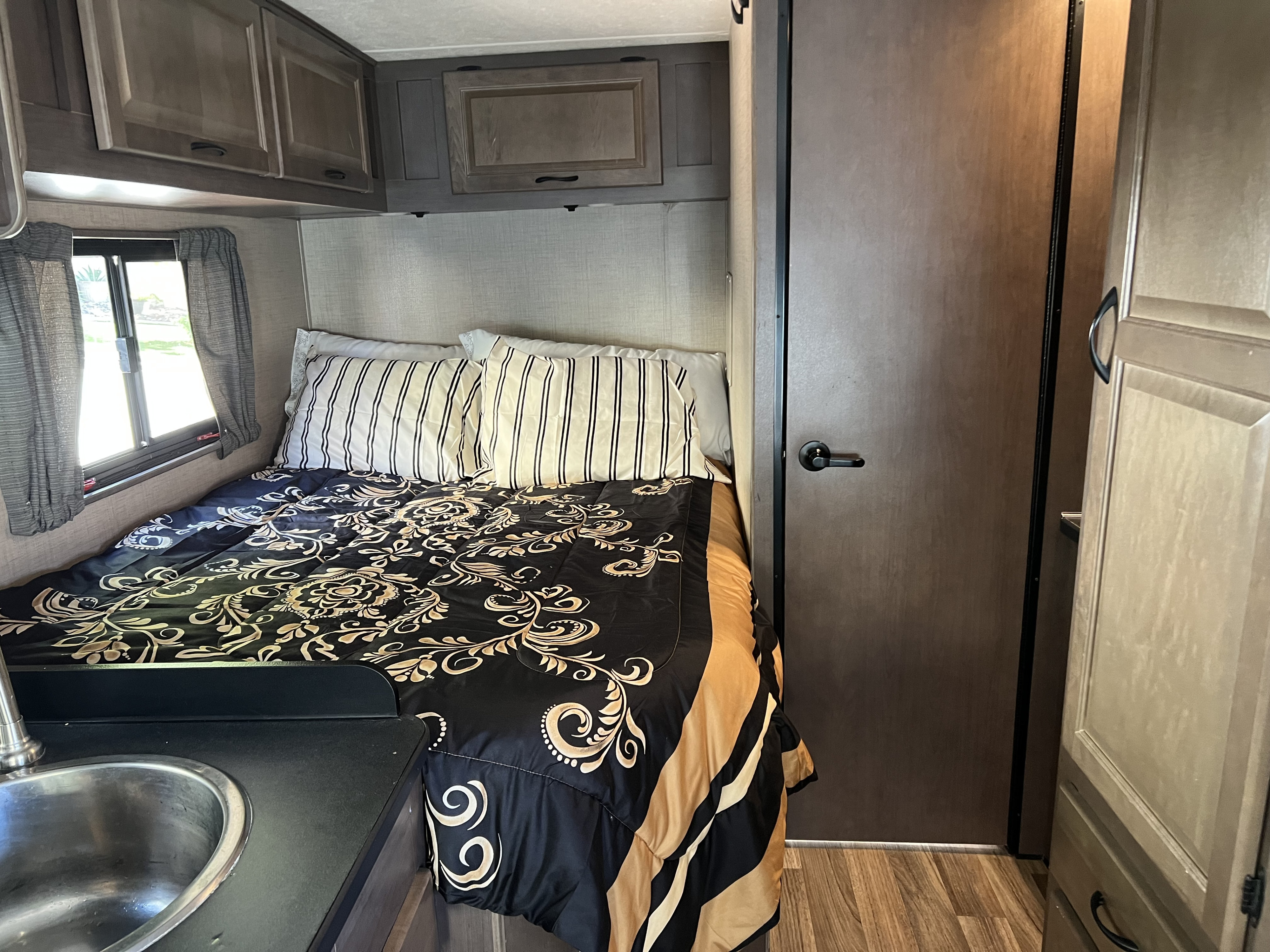 Cozy **RV rental** interior with a patterned bed, overhead cabinets, window, and a small sink for convenience.. Thor Majestic 2019