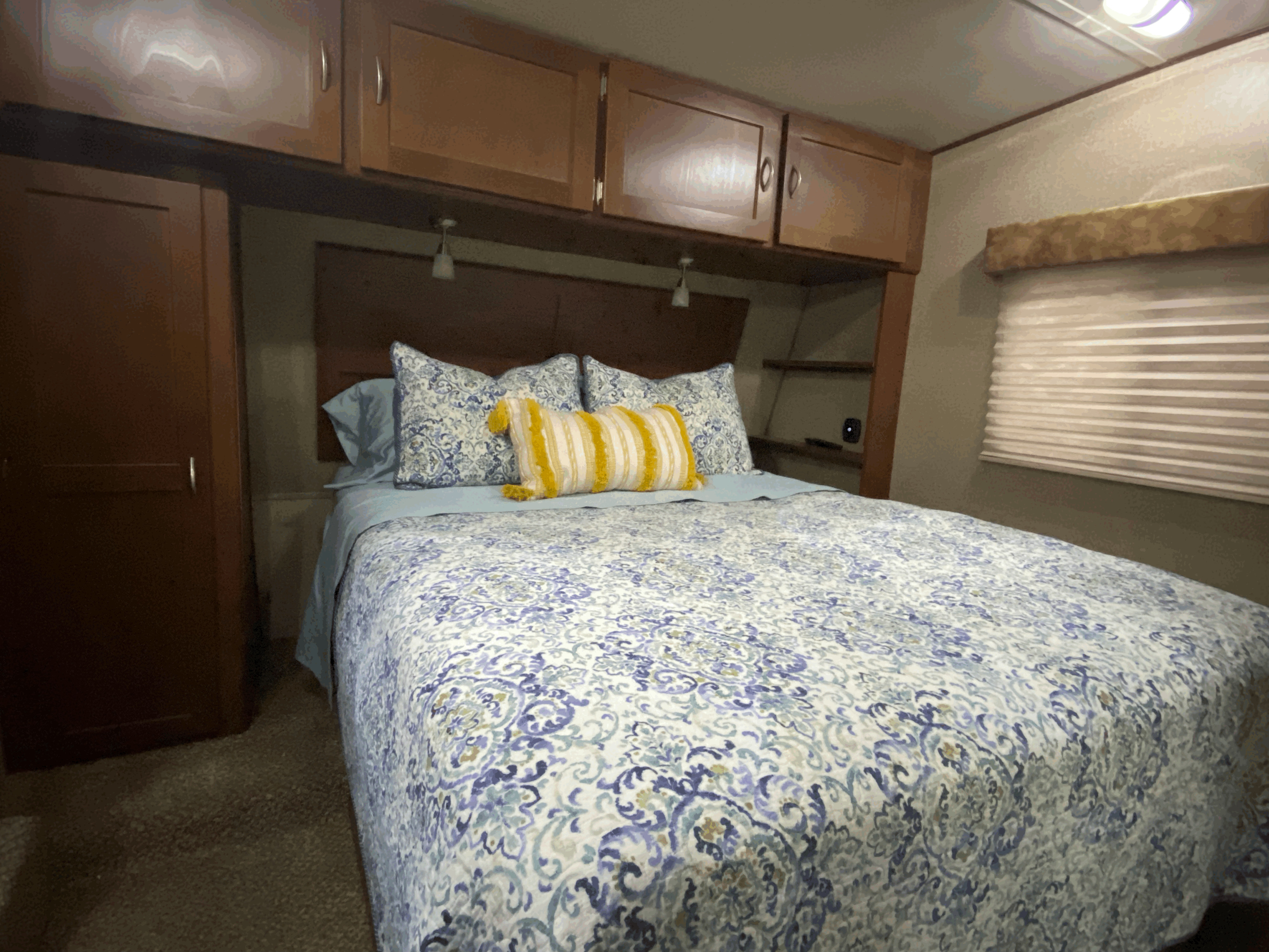Cozy RV rental bedroom features a queen bed with blue & white patterned bedding, yellow accent pillow, and wood cabinets.. Forest River Vengeance 2015