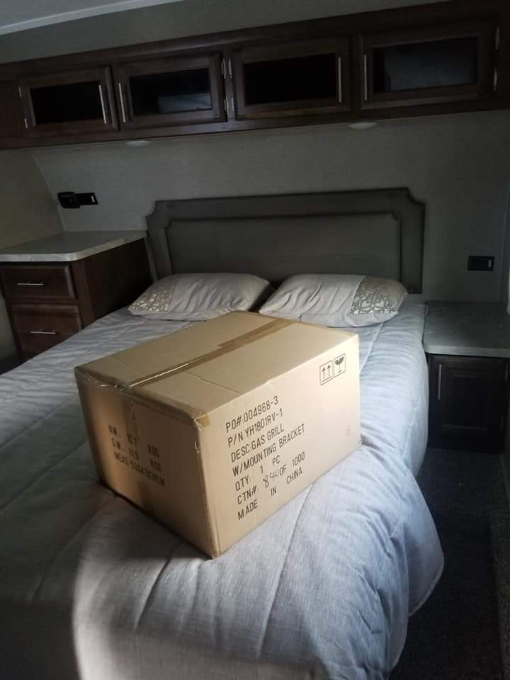 RV rental bedroom: A box on the bed reveals a new gas grill with mounting bracket, for your travel adventures.. Forest River Rockwood Ultra Lite 2019