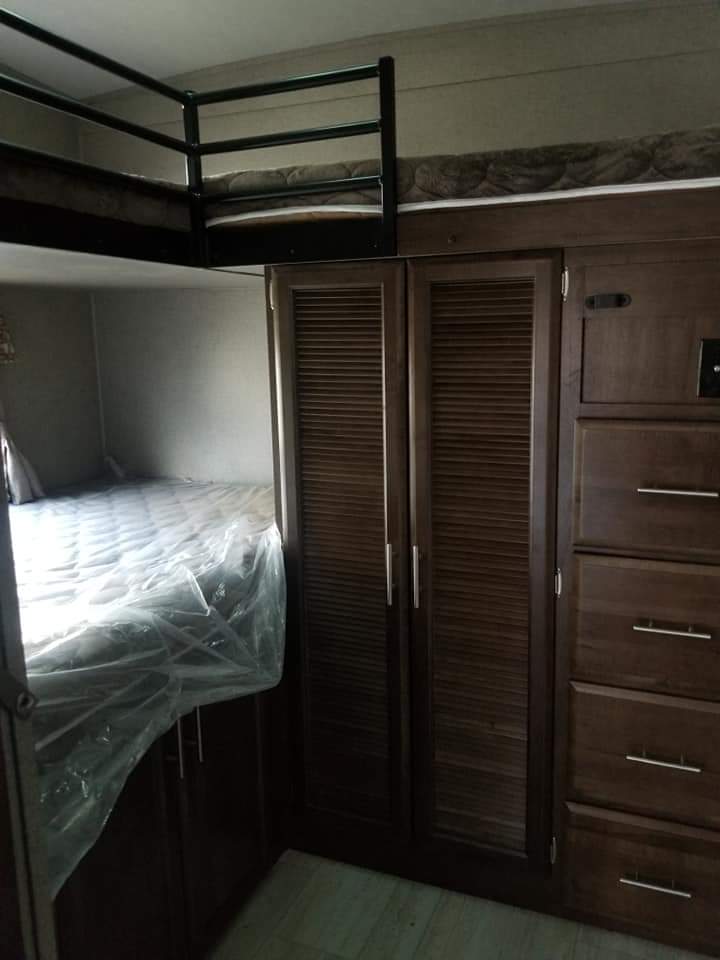 Efficient RV rental bunkhouse: features an upper bunk, lower bed with plastic cover, and dark wood storage cabinets & drawers.. Forest River Rockwood Ultra Lite 2019