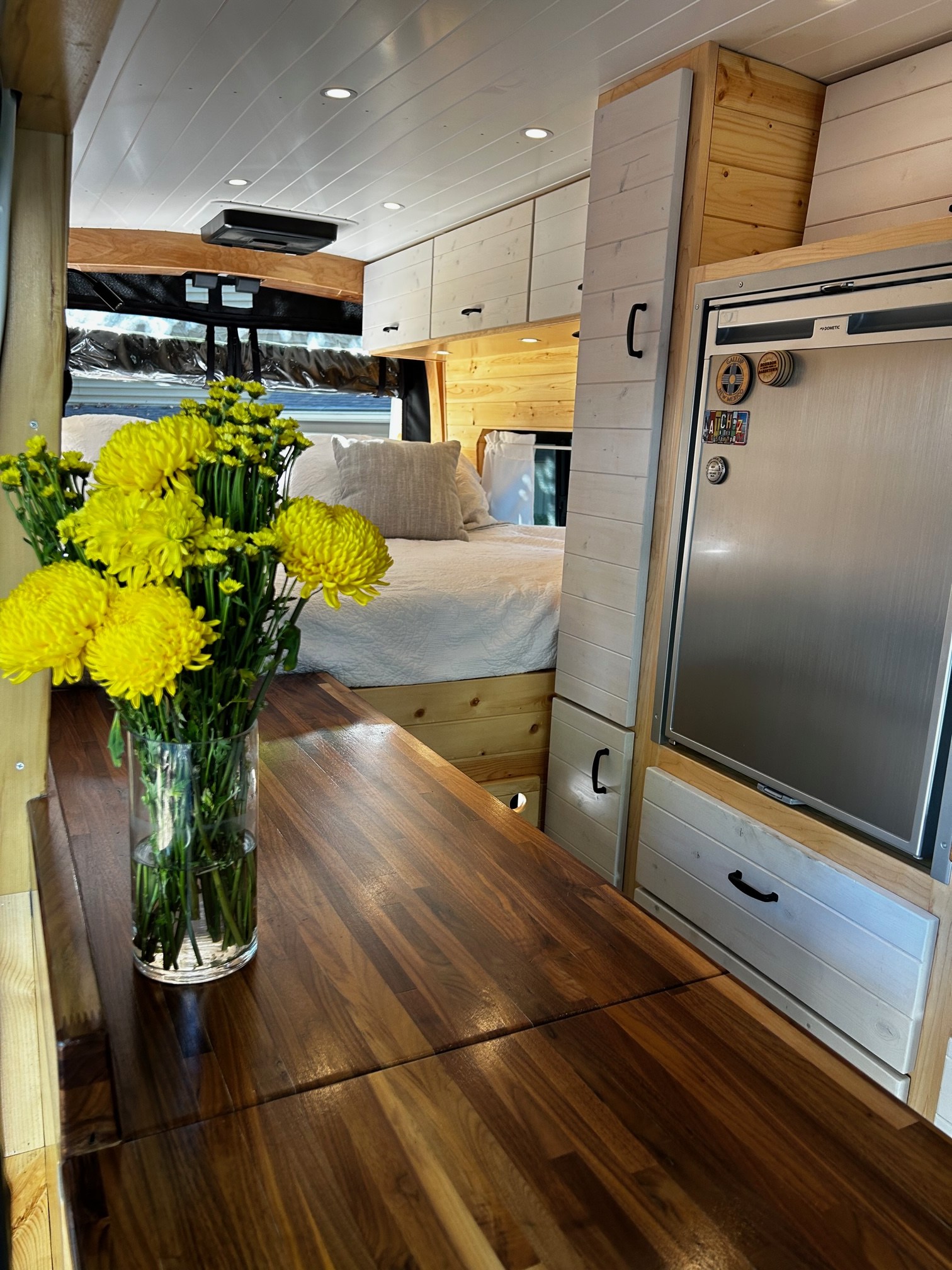RV rental interior: custom wood counters, bright white cabinets, stainless fridge, and a comfy bed. Perfect for van life.. Ford Transit 2020