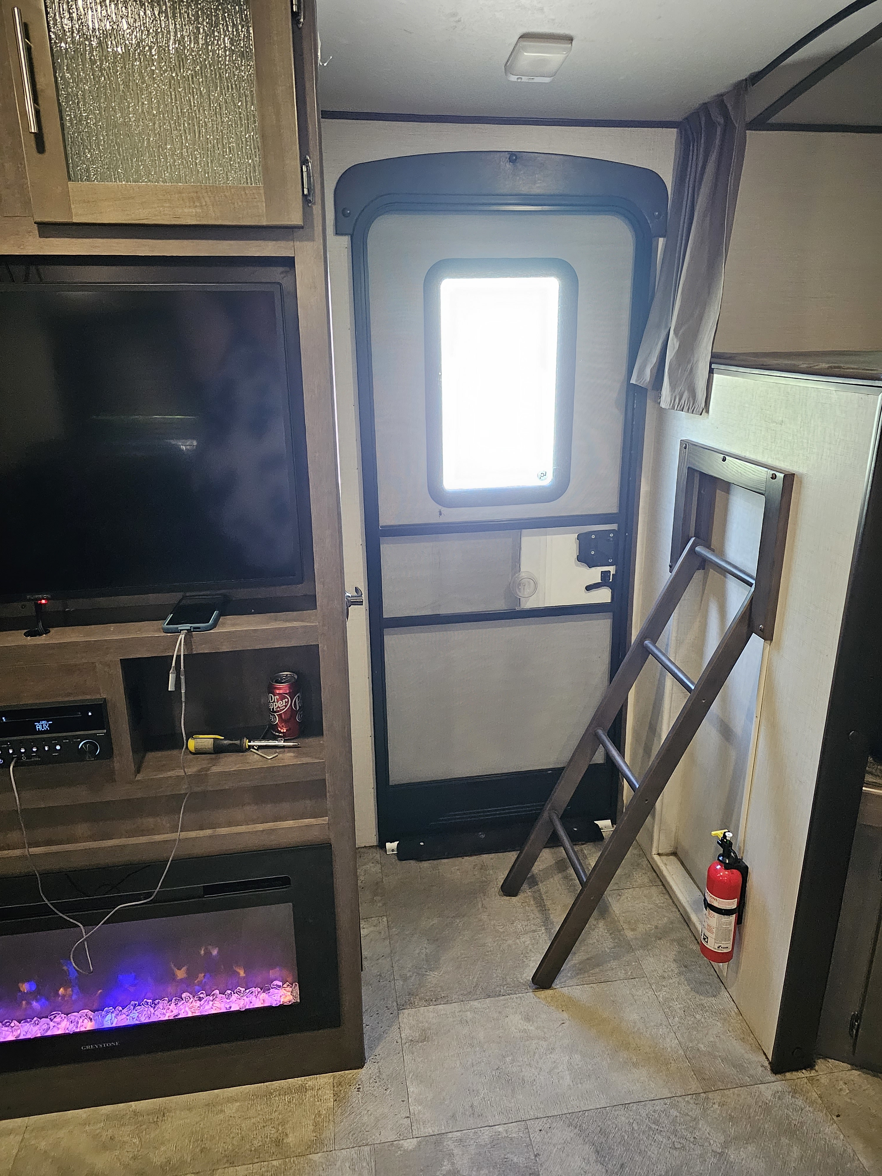 An RV rental interior features a TV entertainment center with fireplace, screen door, and a ladder by the bunks.. Crossroads RV Sunset Trail Grand Reserve 2018