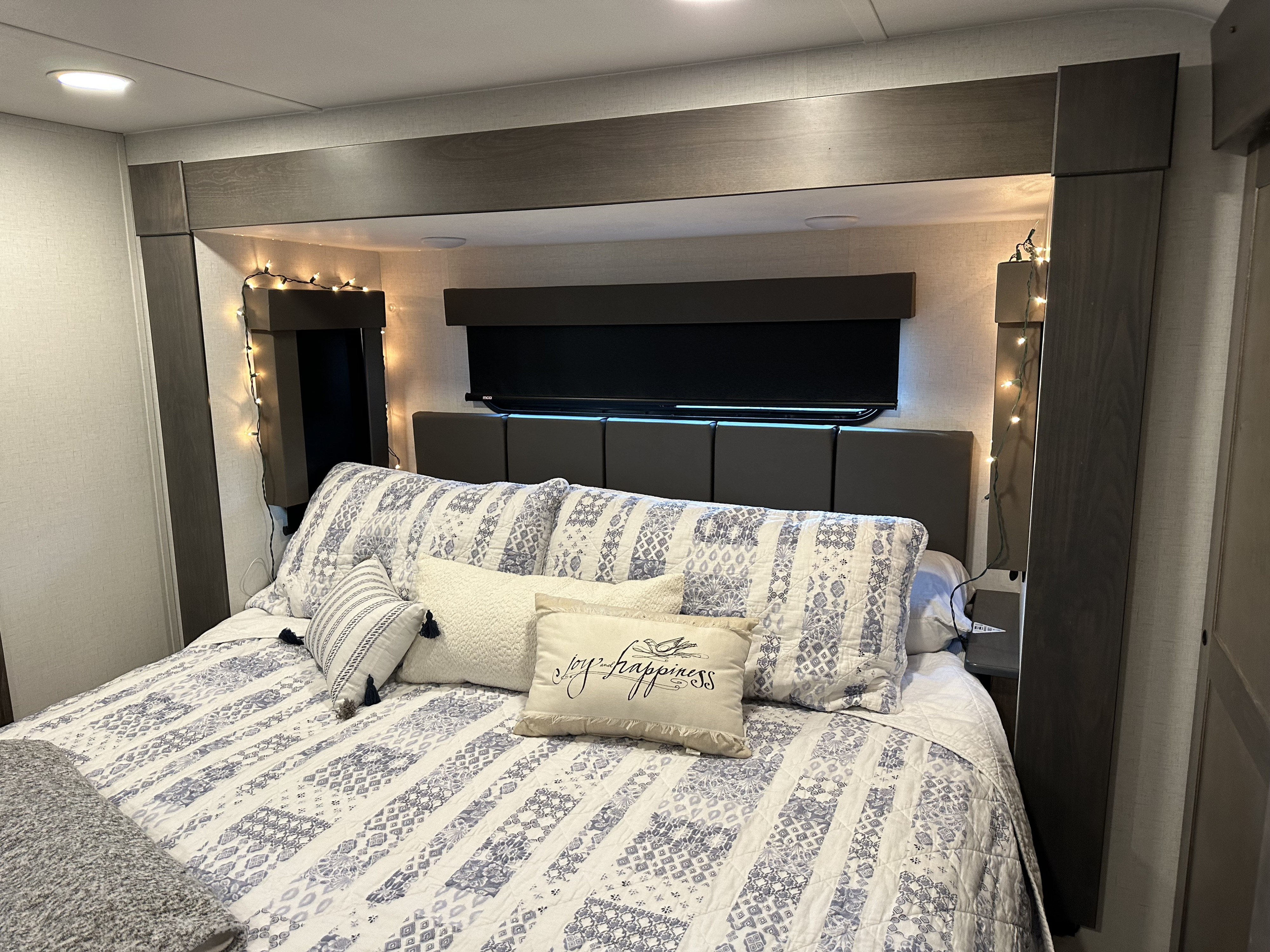 Cozy RV rental bedroom with a comfy bed, decorative pillows, string lights, and a TV for a relaxing stay.. Alliance RV Valor 2023