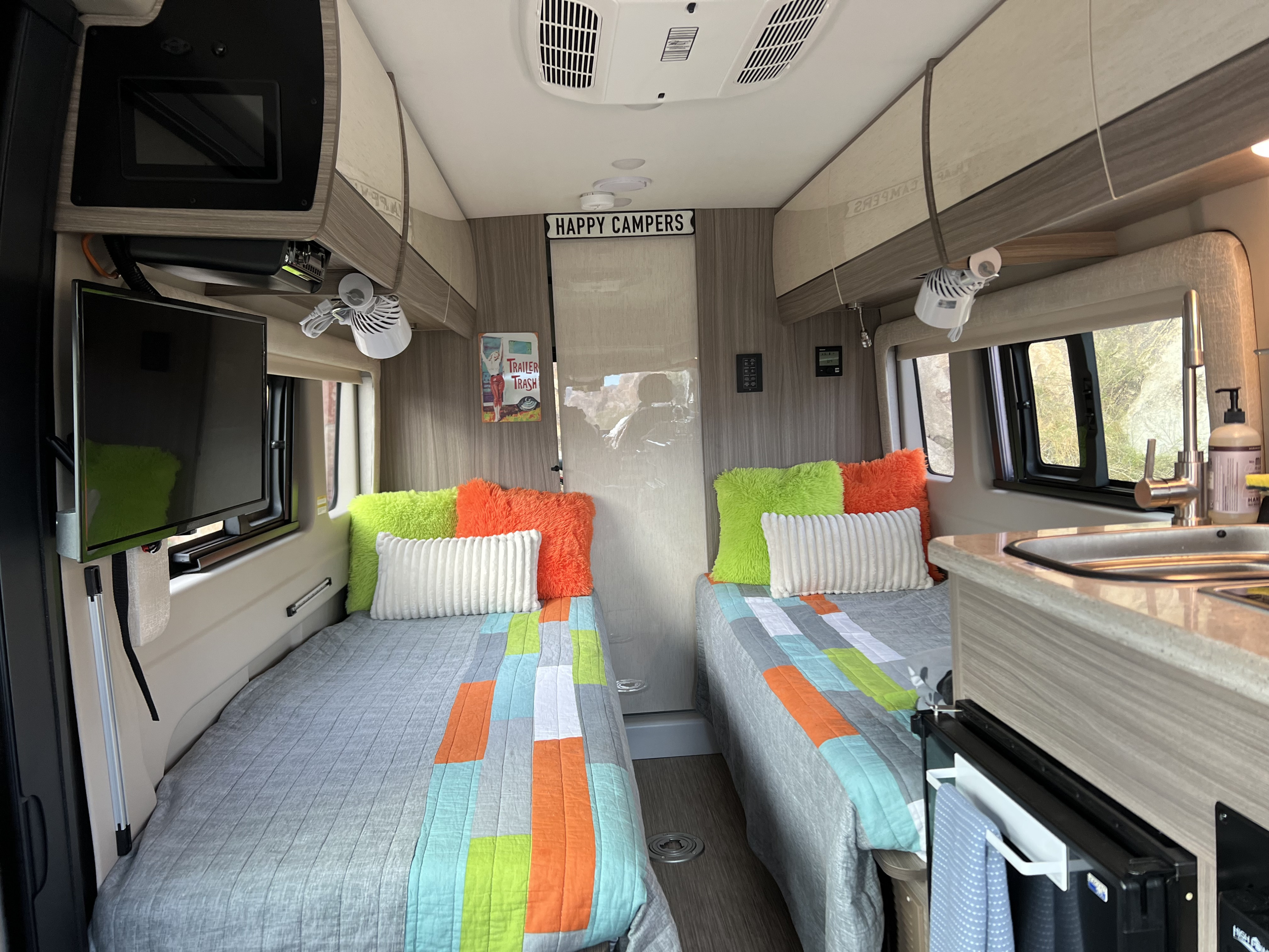 Cozy RV rental interior with twin beds, compact kitchen, TV, and fans, perfect for road trip comfort.. Jayco Swift 2023