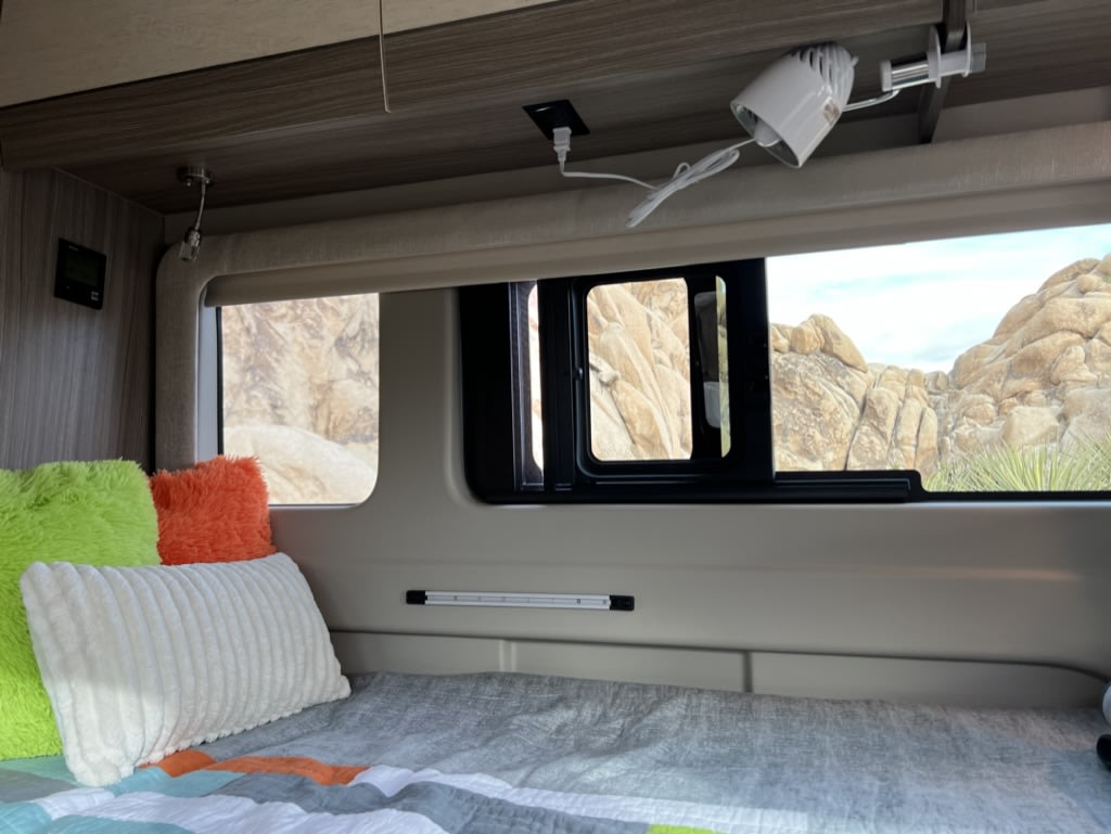 Cozy RV rental interior with a bed, colorful pillows, and window view of desert rock formations. Perfect for nature travel.. Jayco Swift 2023