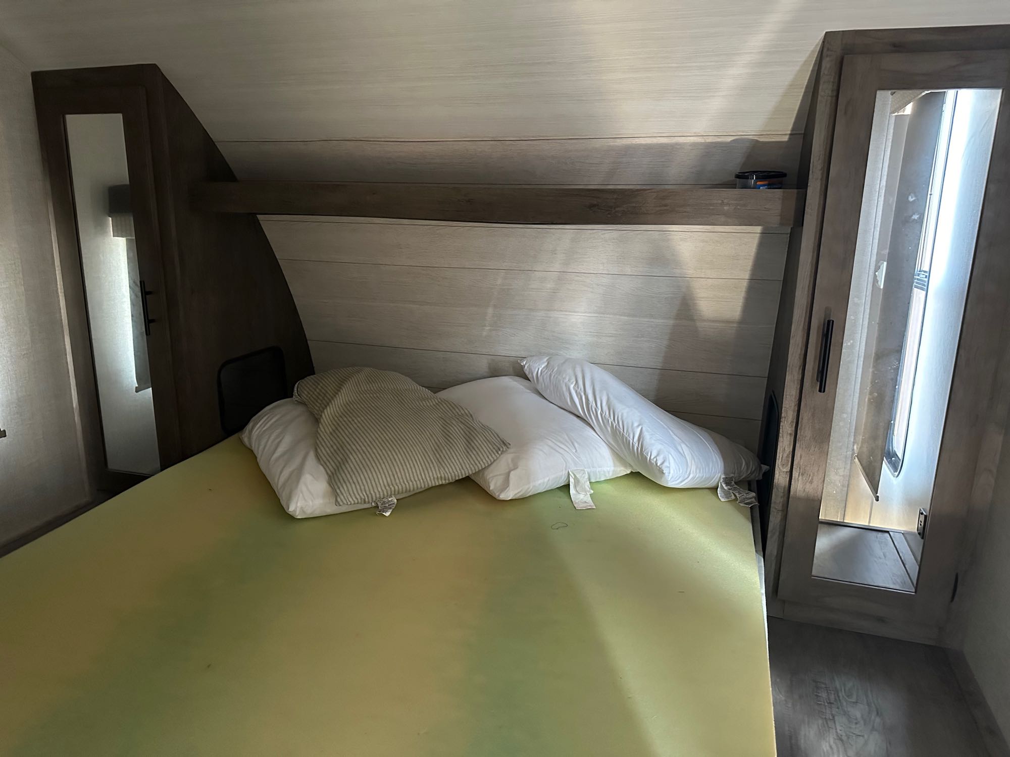 RV rental bedroom view: A bed with light green mattress and pillows, surrounded by light wood paneling and cabinetry.. Forest River Salem Cruise Lite 2021
