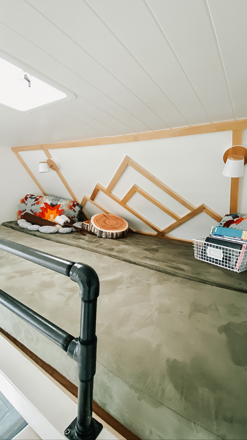 Cozy RV rental bunk bed loft with mountain wall decor, camping pillows, and reading lights for a comfy adventure.. Four Winds Chateau 2004