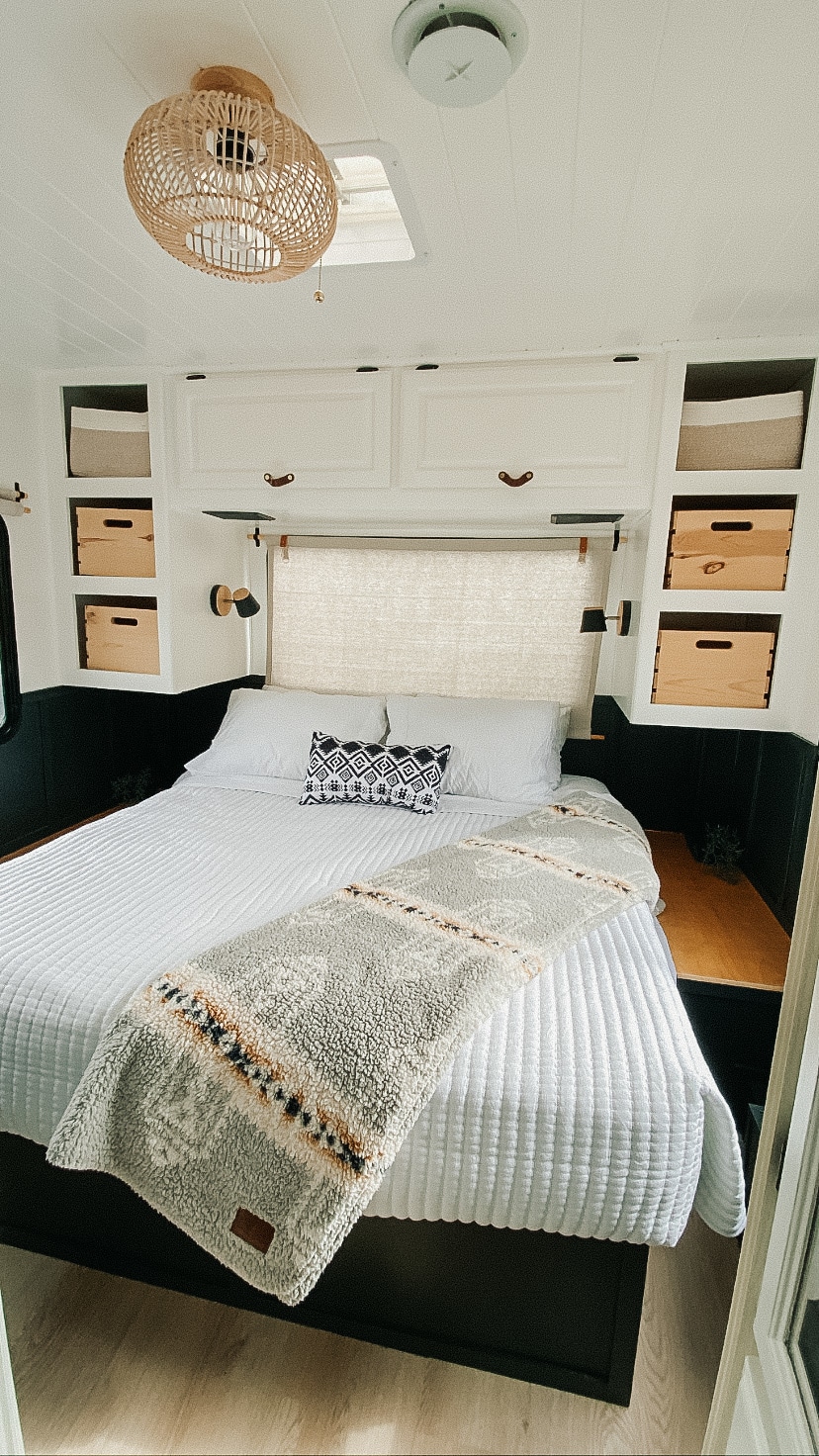 Cozy RV rental bedroom features white bedding, patterned throw, ample overhead storage, and a rattan light.. Four Winds Chateau 2004