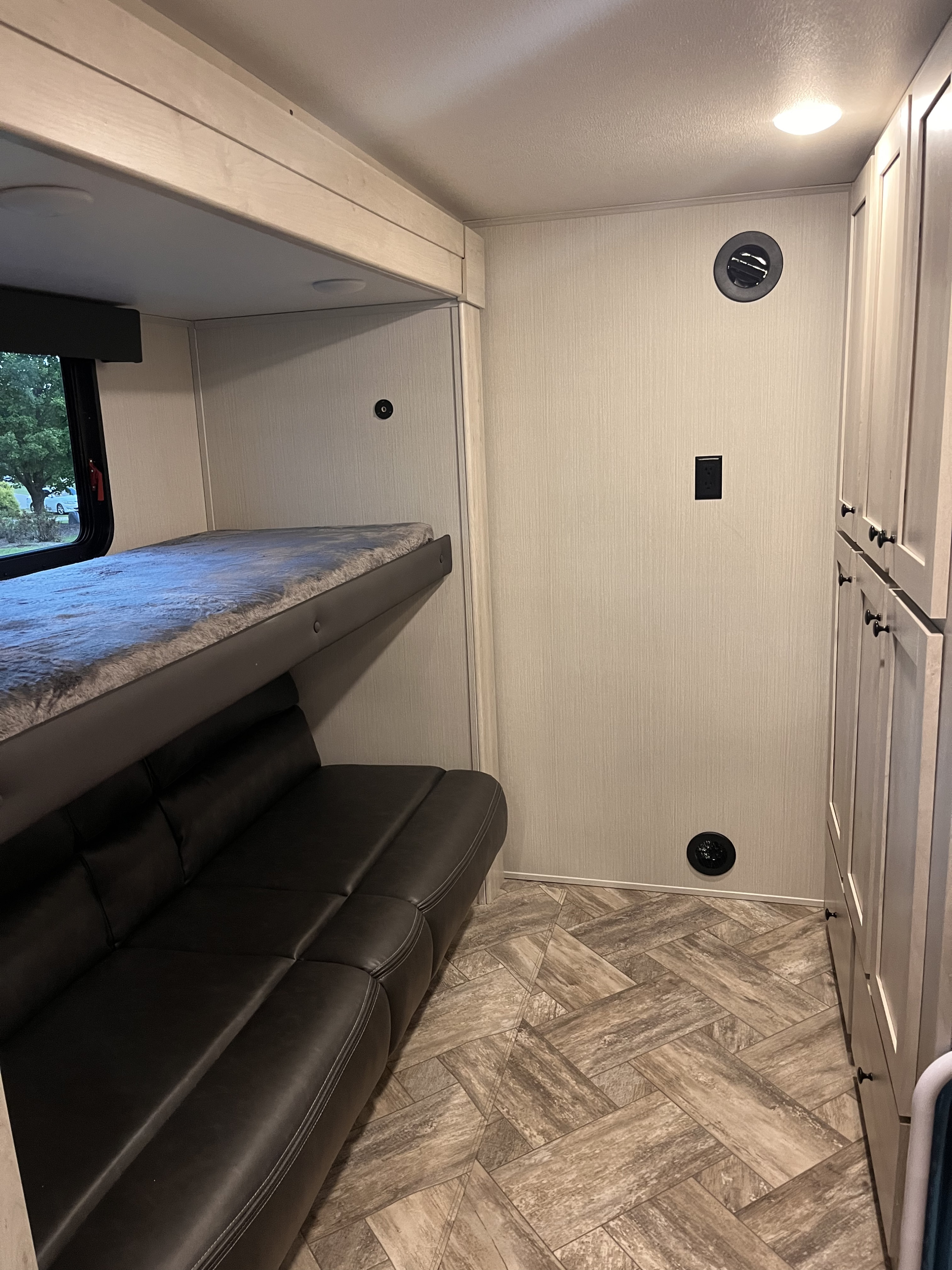 RV rental interior features bunk bed, sofa, light-toned cabinets, and herringbone floor pattern.. Forest River Wildcat 2023