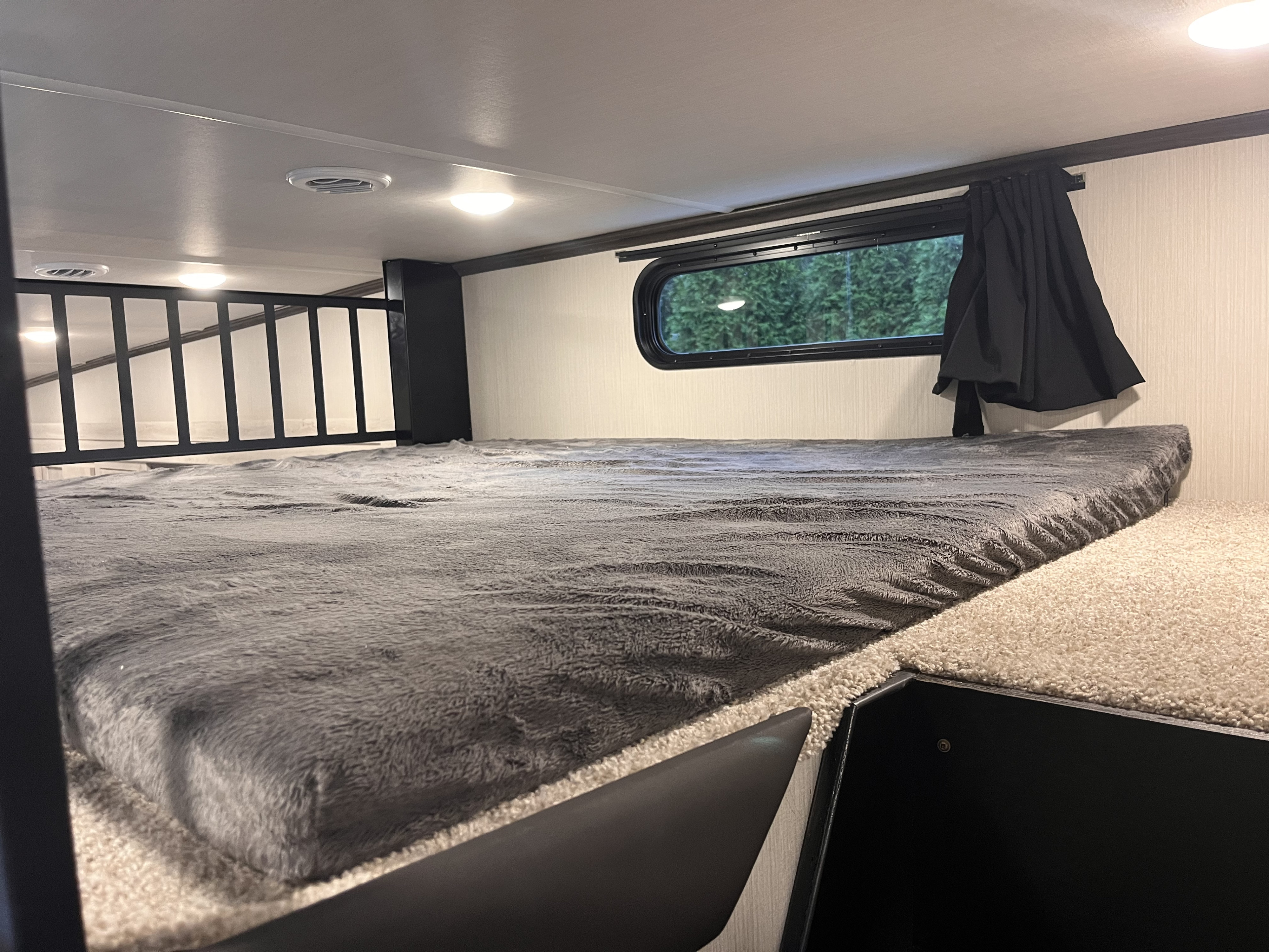 Inside an RV rental: a cozy bunk bed with a gray blanket, small window, and protective railing.. Forest River Wildcat 2023