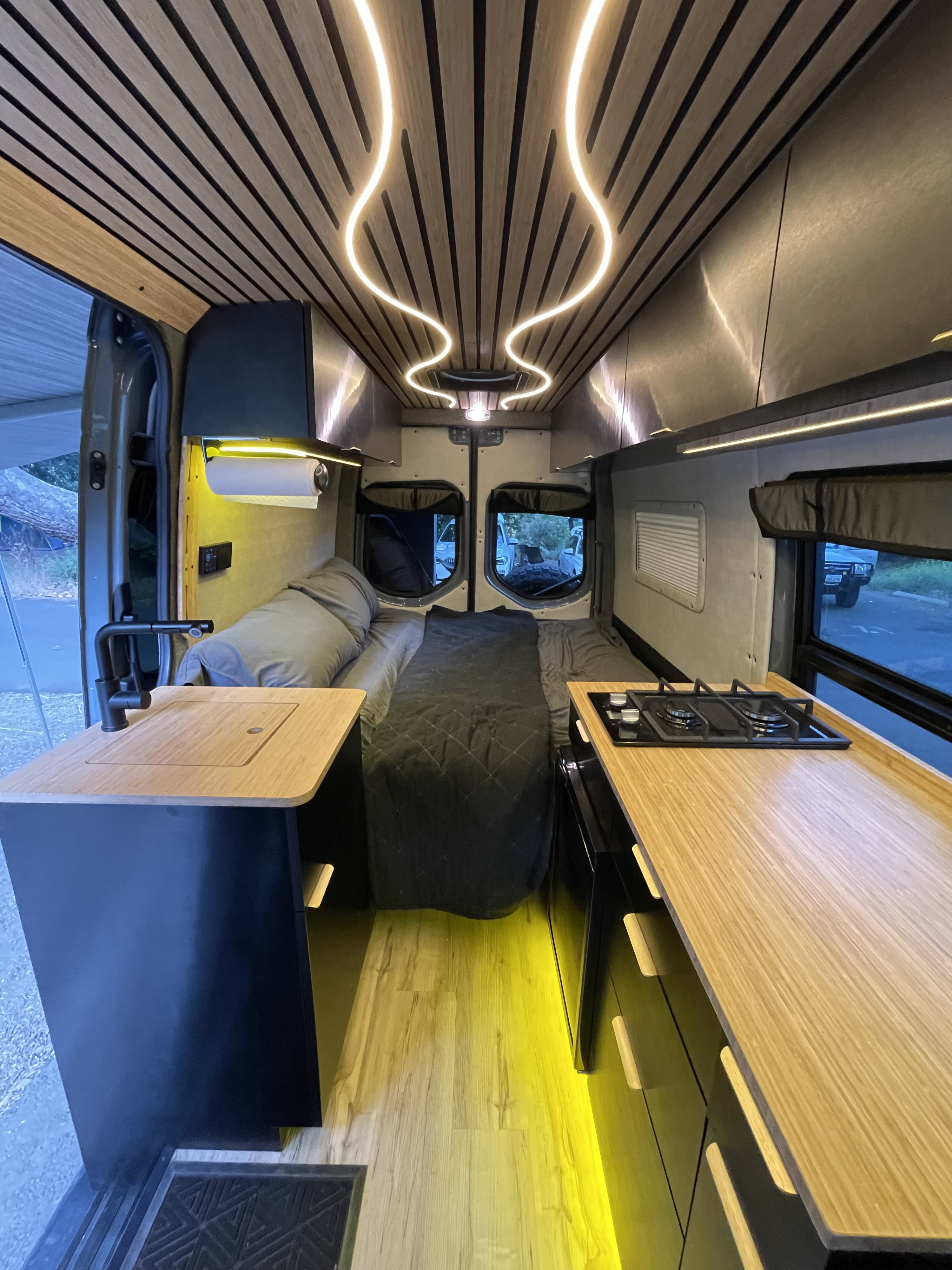 Explore this high-end RV rental's interior! Features a modern wood ceiling with curved LEDs, a full kitchen, and comfortable bed.. Mercedes-Benz Sprinter RV Motorhome Campervan 2020
