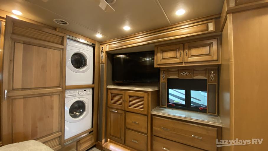 Luxury RV rental interior with stacked washer/dryer units, flat-screen TV, and rich wood cabinetry, offering home comforts.. Tiffin QKH 2018
