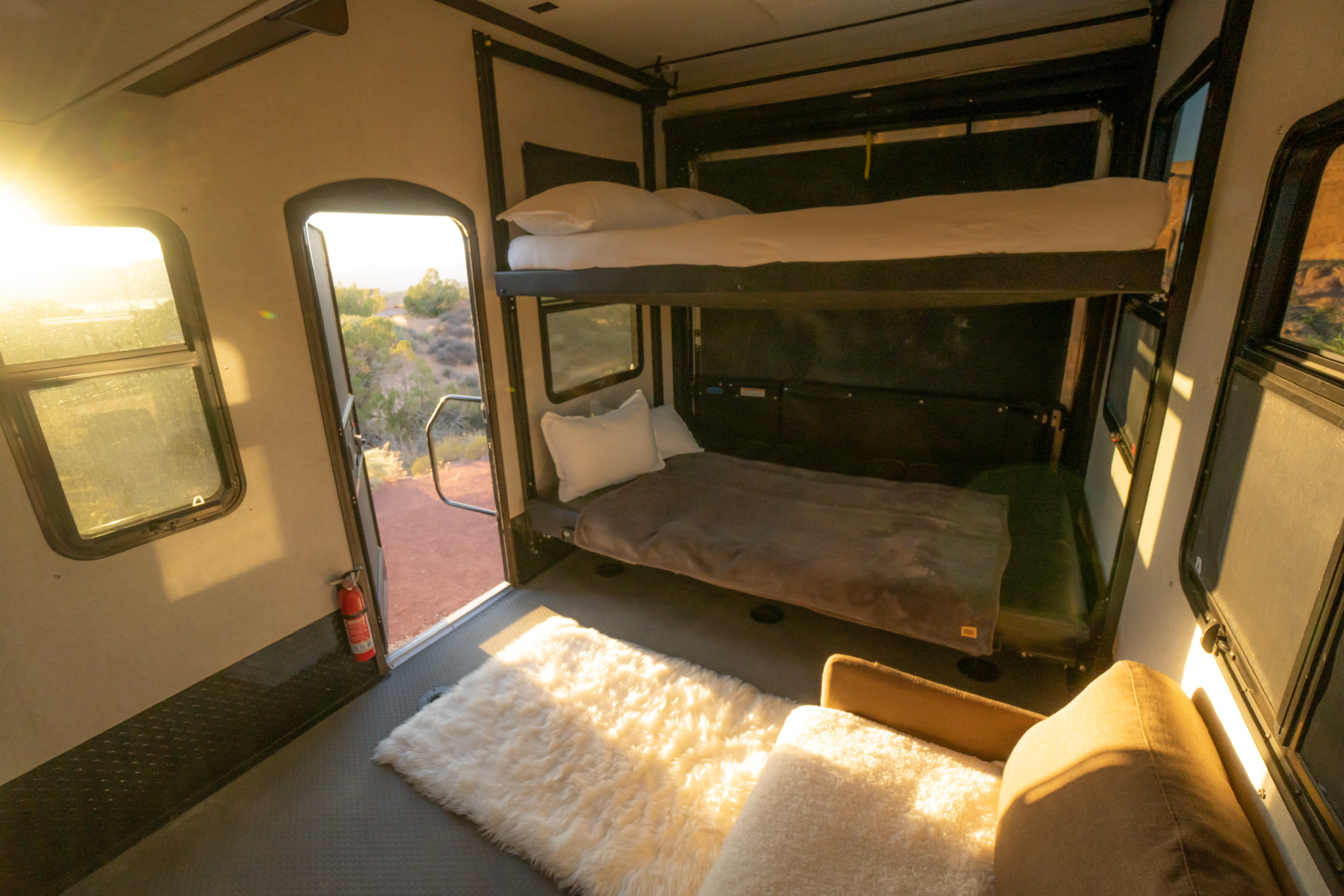 RV rental interior with bunk beds, a cozy rug, and a door opening to a sunlit desert view, ideal for adventures.. Keystone RV Raptor Toy Hauler 2019