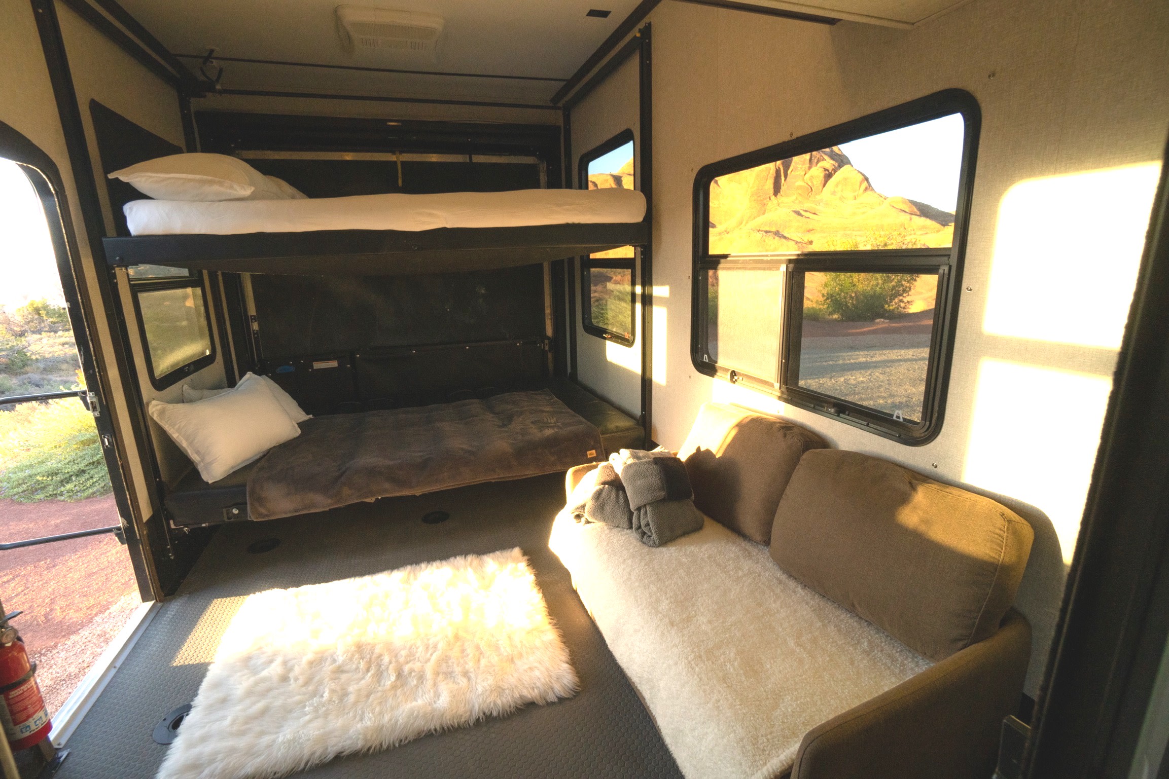 Inside an RV rental: bunk beds, a comfortable sofa, and bright desert views out the windows.. Keystone RV Raptor Toy Hauler 2019