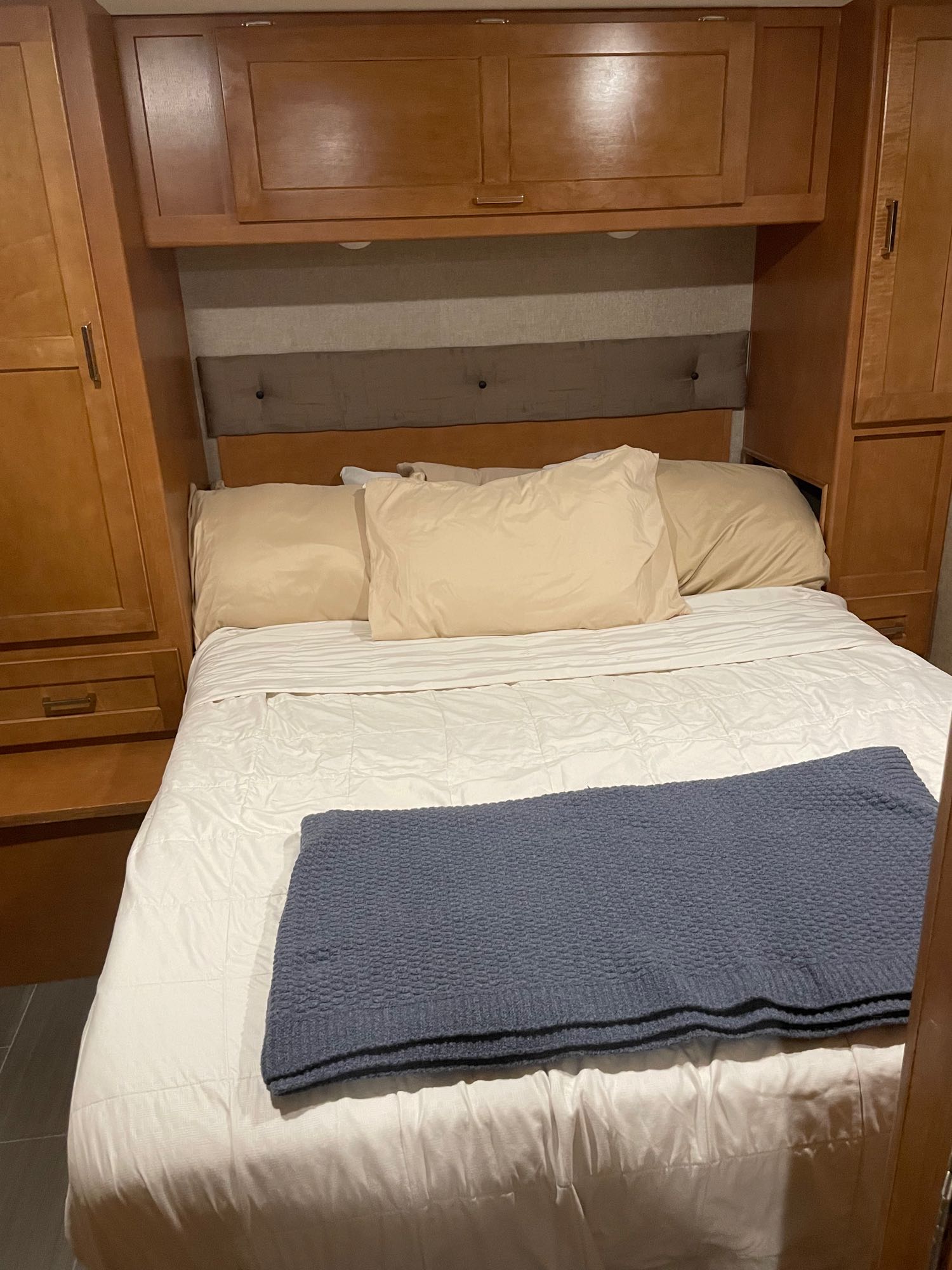 Cozy bedroom in an RV rental, featuring a bed with neutral linens, a blue throw, and built-in storage.. Winnebago Minnie Winnie 2018