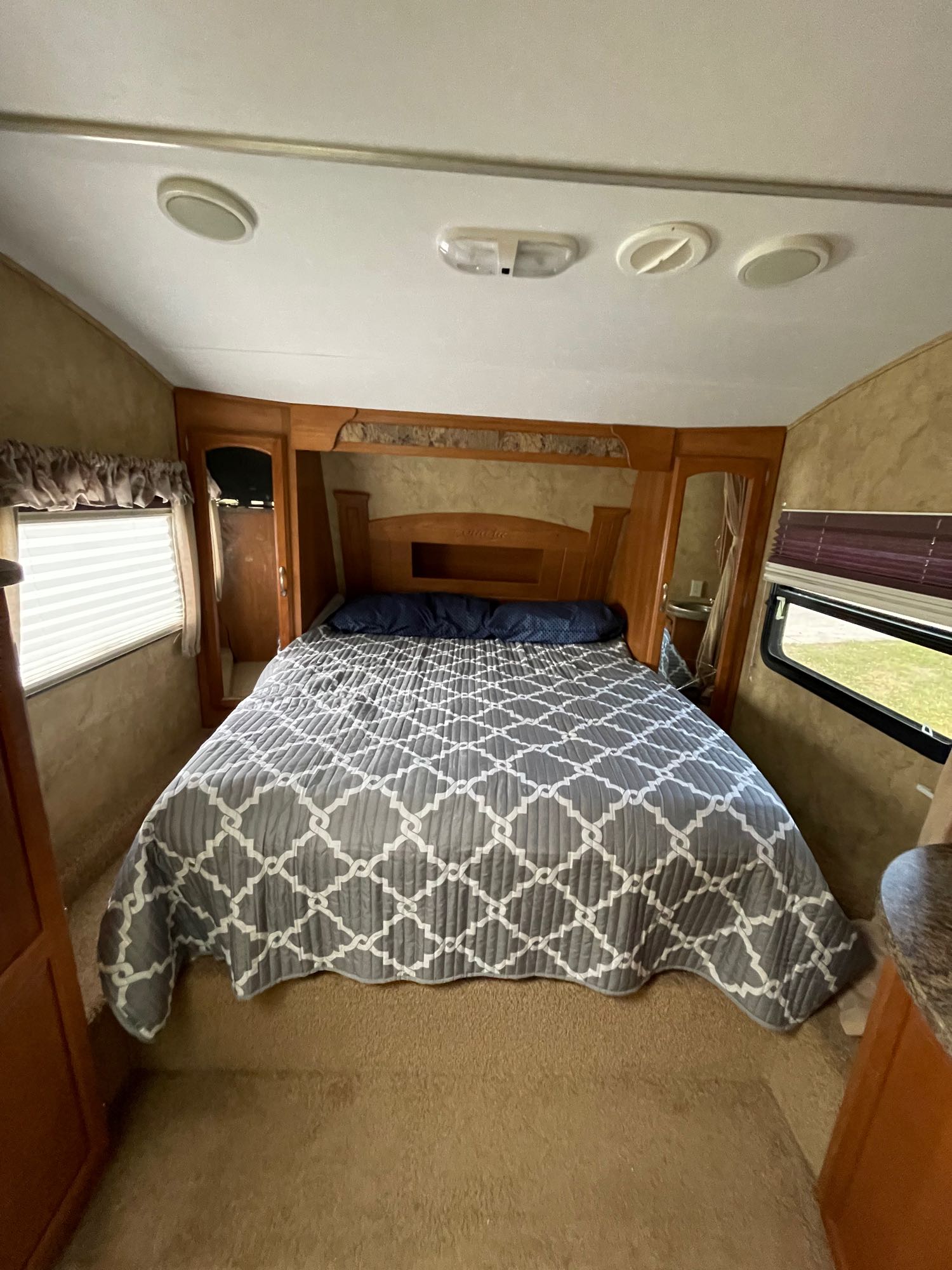 Cozy RV rental bedroom featuring a full bed with a gray quilt, built-in storage, and side windows.. Keystone RV Cougar 2012