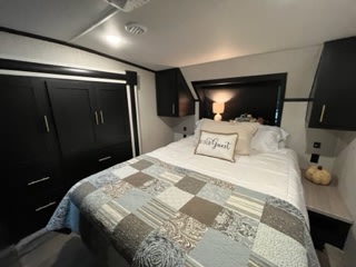 Comfortable RV rental bedroom featuring a queen bed with quilt, nightstands, and dark storage cabinets. Ready for your travels!. Forest River Wildcat 2022