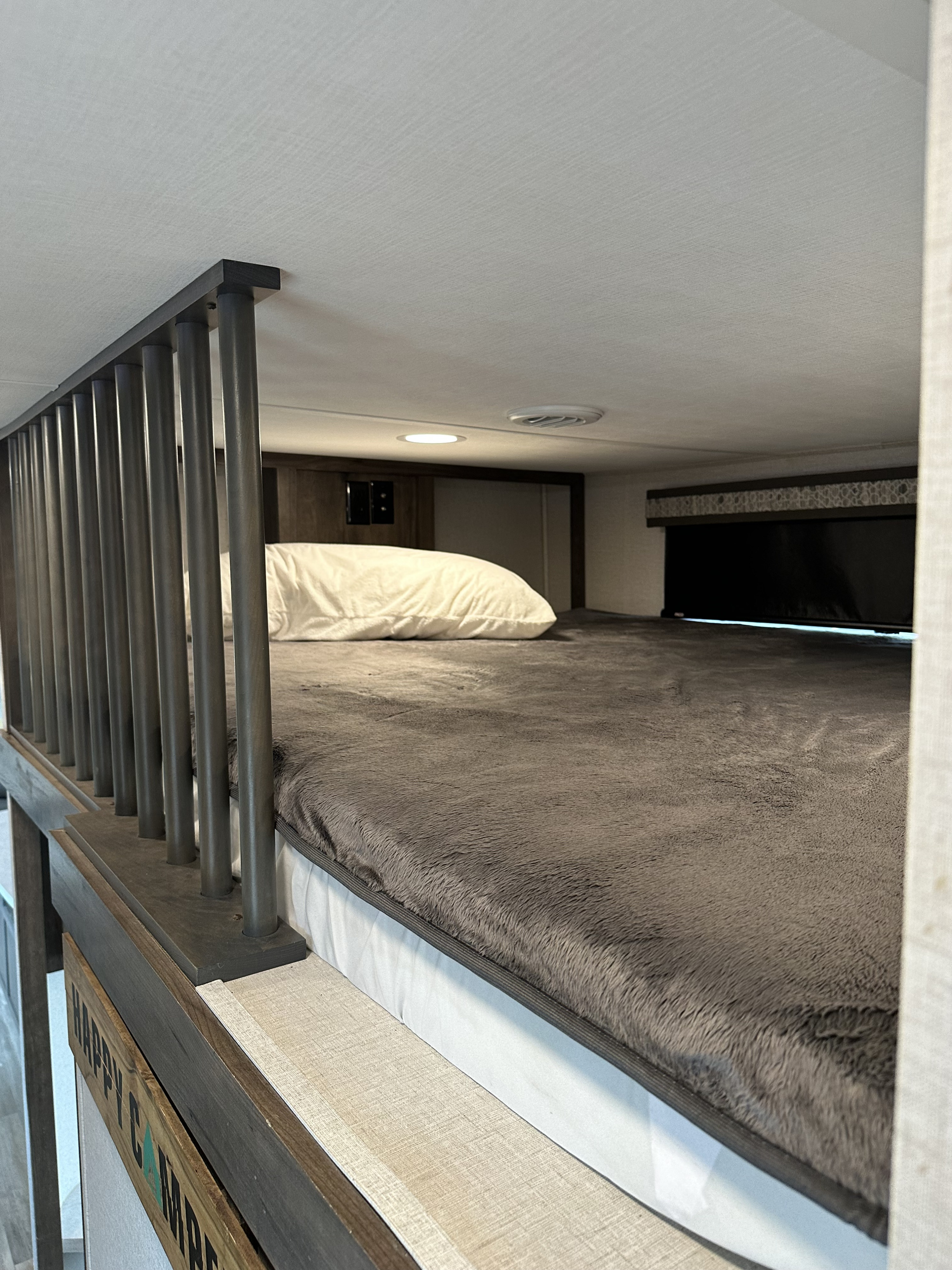 This RV rental's cozy bunk bed features a soft, gray blanket, white pillow, and a safety railing. Overhead light and vent visible.. Alliance RV Paradigm 2021