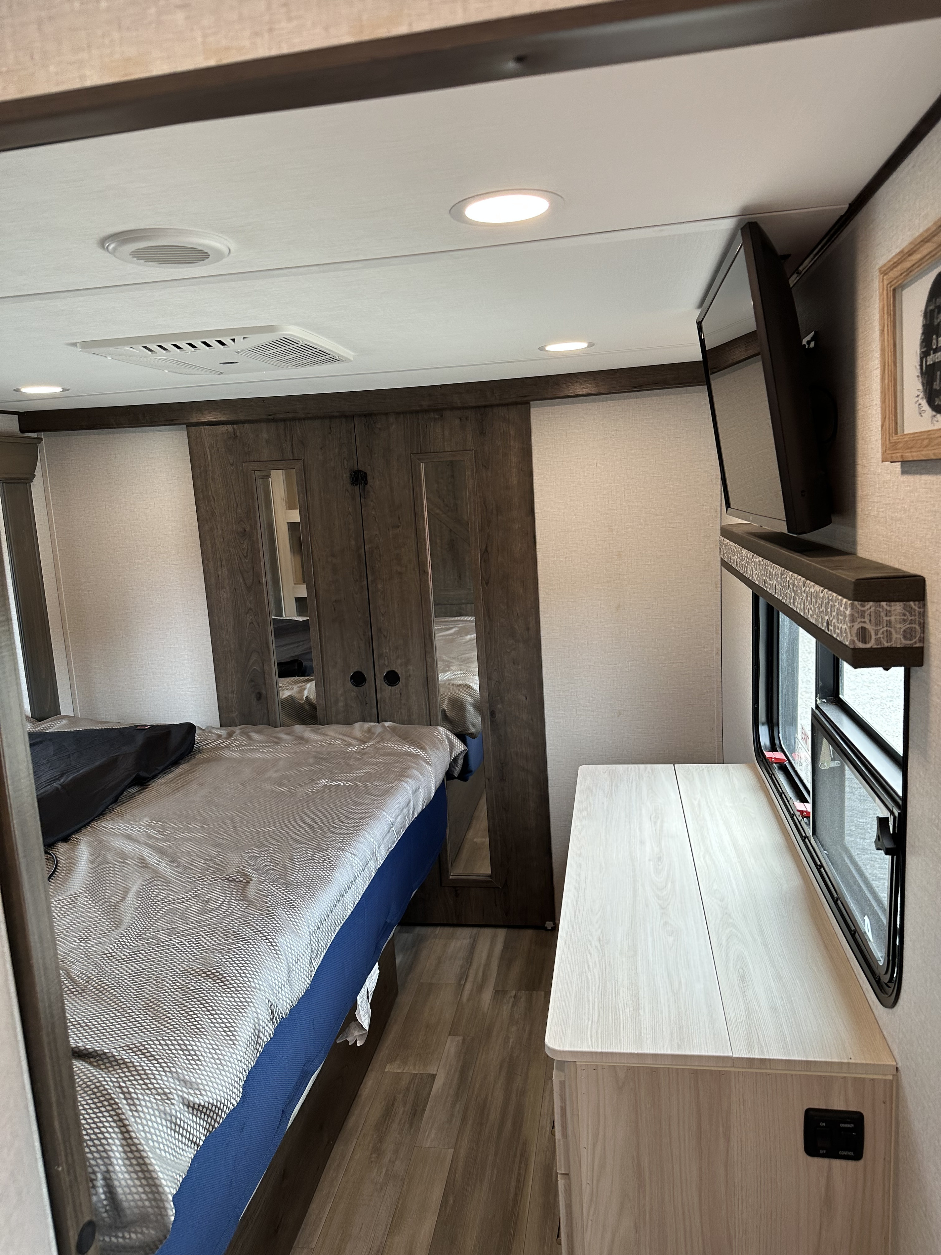 Inside an RV rental, a cozy bedroom with a bed, mirrored closet, TV, and a dresser by the window, designed for travel comfort.. Alliance RV Paradigm 2021