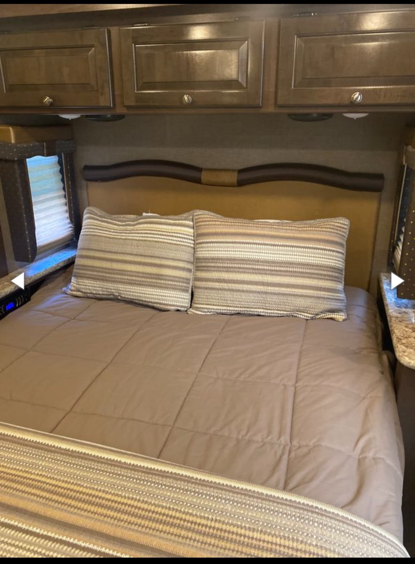 Relax in this inviting RV rental bedroom. A comfortable bed with striped pillows, overhead cabinets, and a window are shown.. Thor Windsport 2018