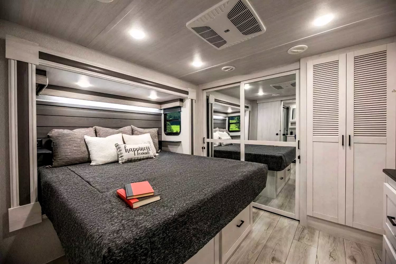 Comfortable RV rental bedroom featuring a cozy bed with storage, mirrored closet, and a bright, modern interior.. East to West Ahara 2022