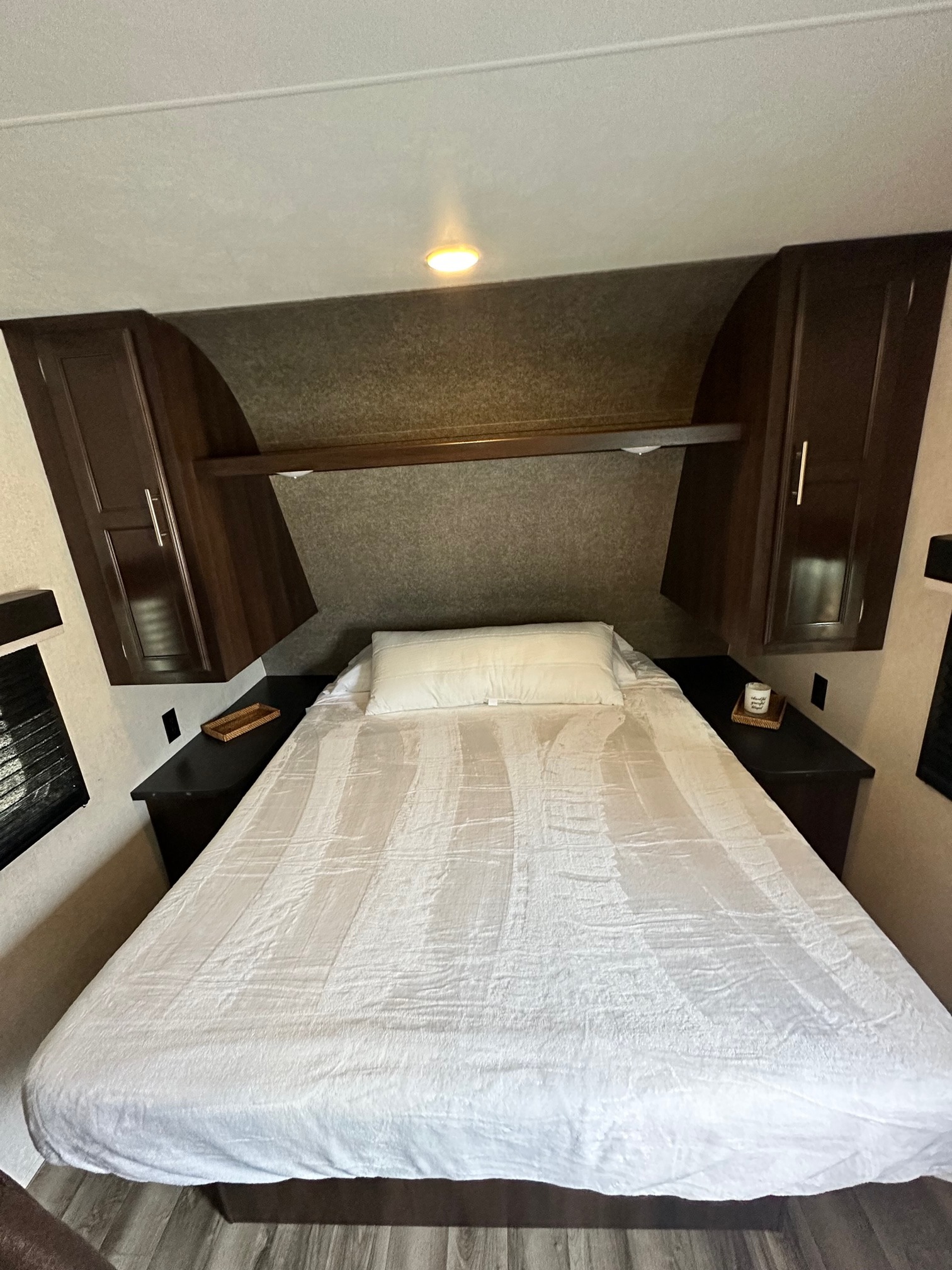 This RV rental's cozy bedroom features a white queen bed, dark wood overhead cabinets, and convenient side storage.. Jayco Jay Flight SLX 2020