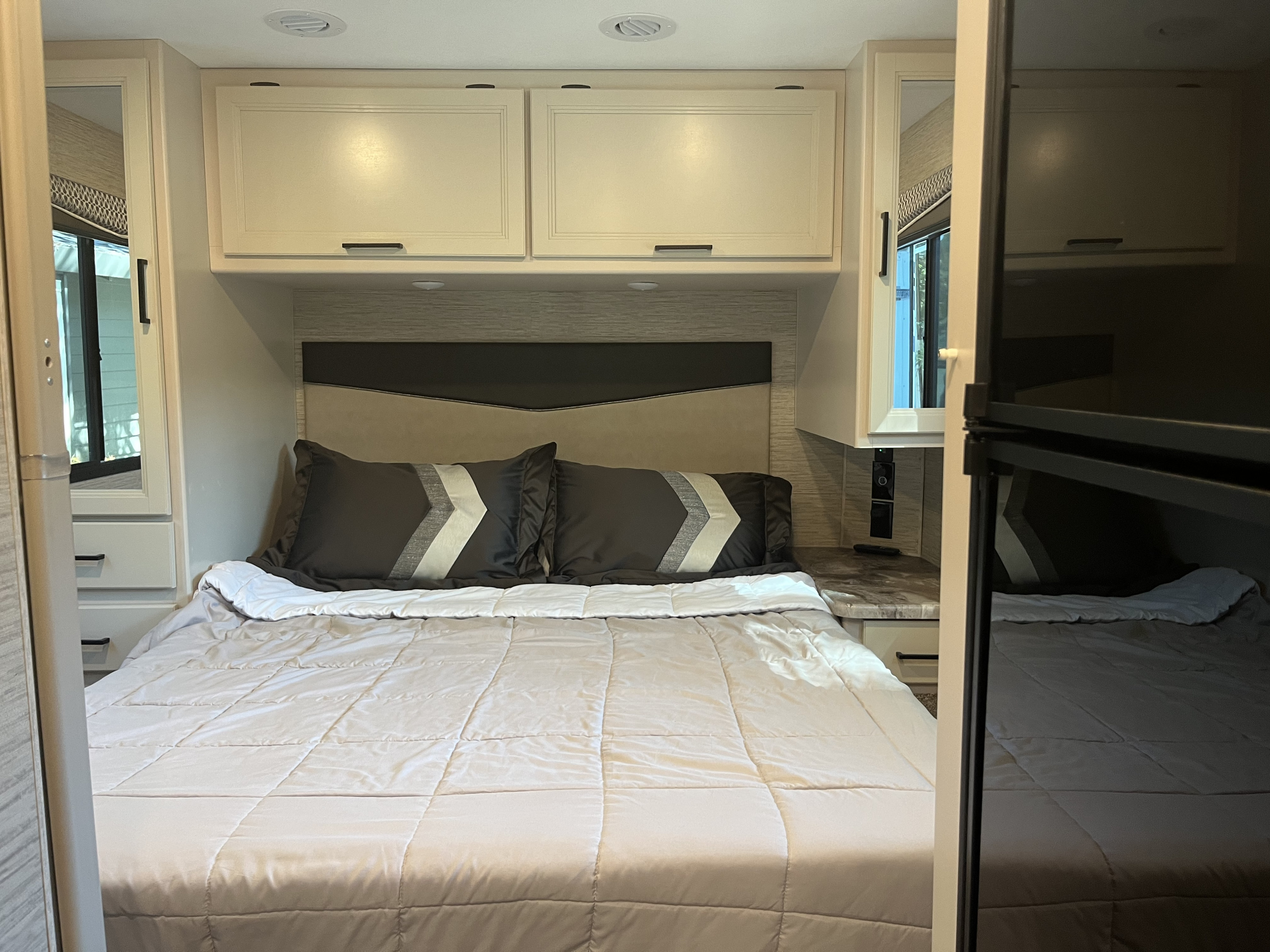 Spacious RV rental bedroom with a large comfortable bed, overhead cabinets, and built-in storage for travel comfort.. Thor Four Winds 2023