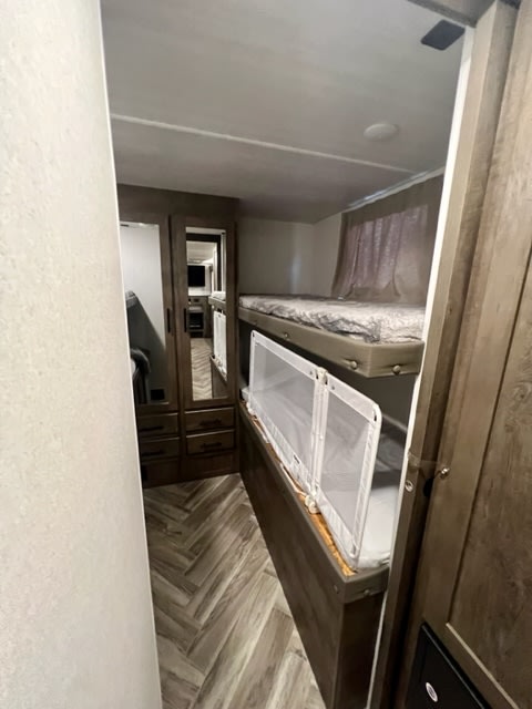 RV rental interior featuring cozy bunk beds with safety netting, a mirrored dresser, and attractive herringbone flooring.. Forest River Salem Cruise Lite 2021