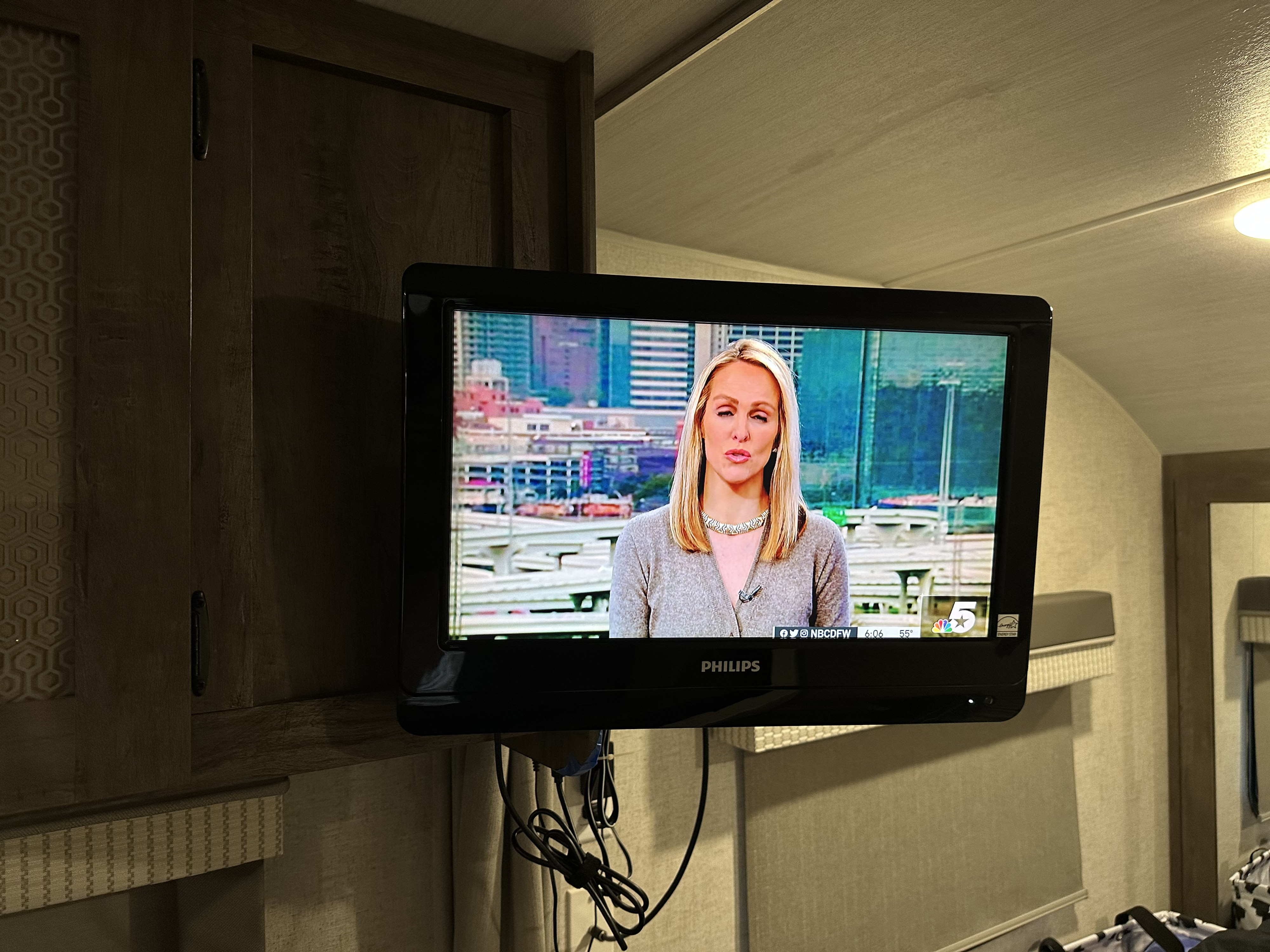 An RV rental's interior features a mounted Philips TV showing a news anchor. Wood cabinets, patterned walls, and visible cables complete the scene.. Forest River Salem Cruise Lite 2021