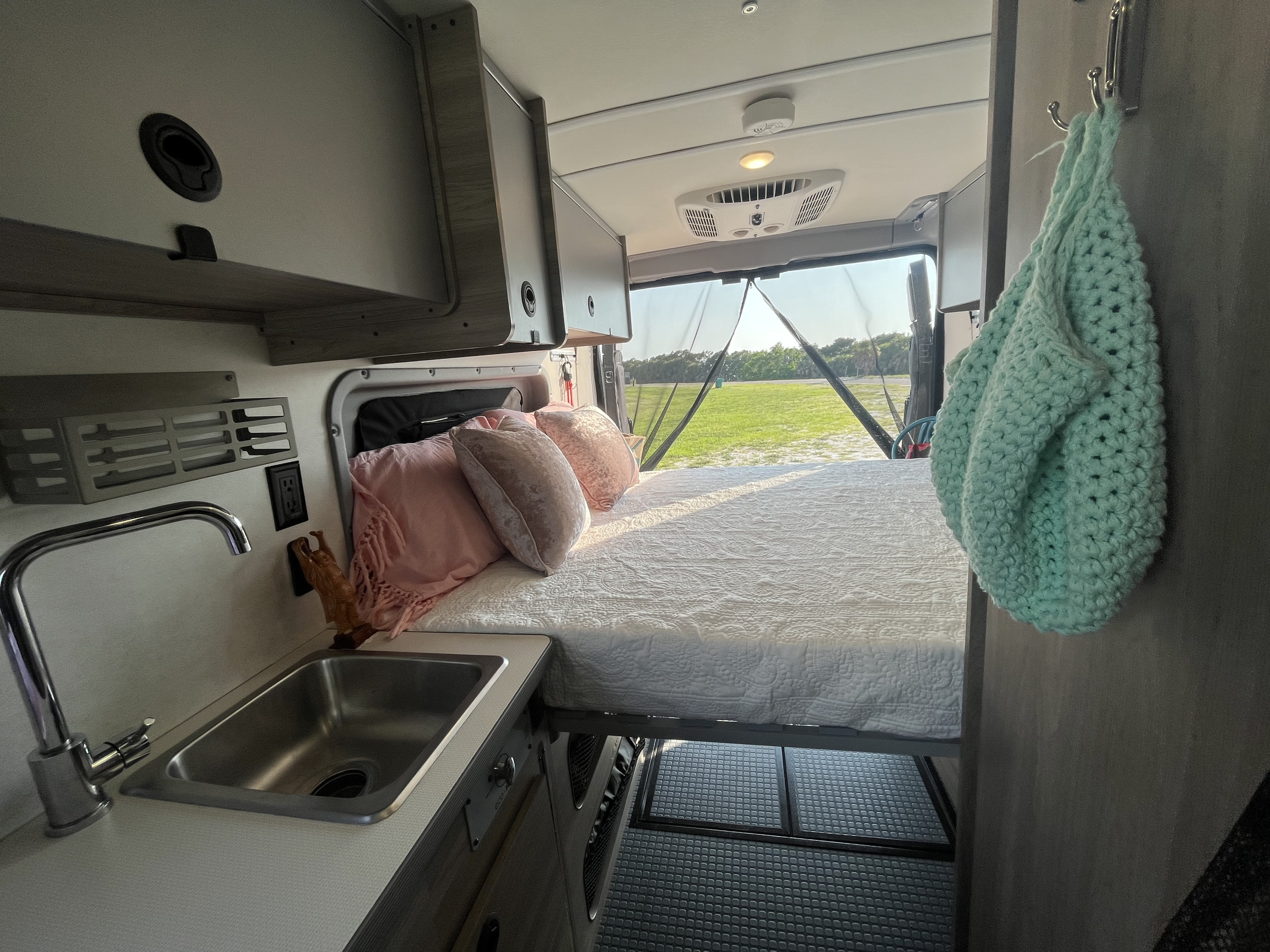 RV rental interior: comfy bed, compact sink, and outdoor view through the back screen.. Winnebago Solis 59PX 2021