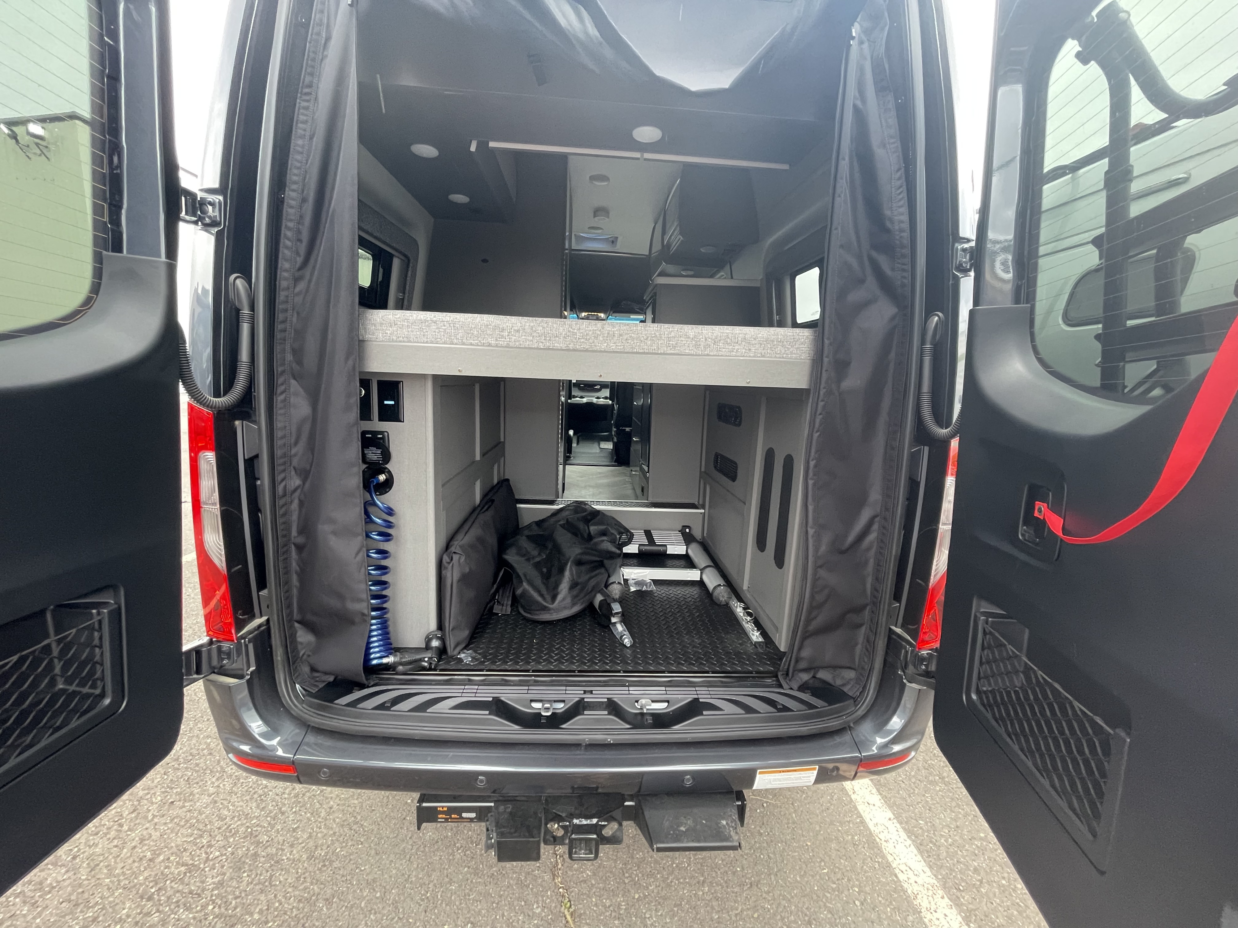 Spacious RV rental camper van interior with rear doors open, showing bed, storage, and utility hookups. Perfect for adventure!. THOR MOTOR COACH Tranquility 2024