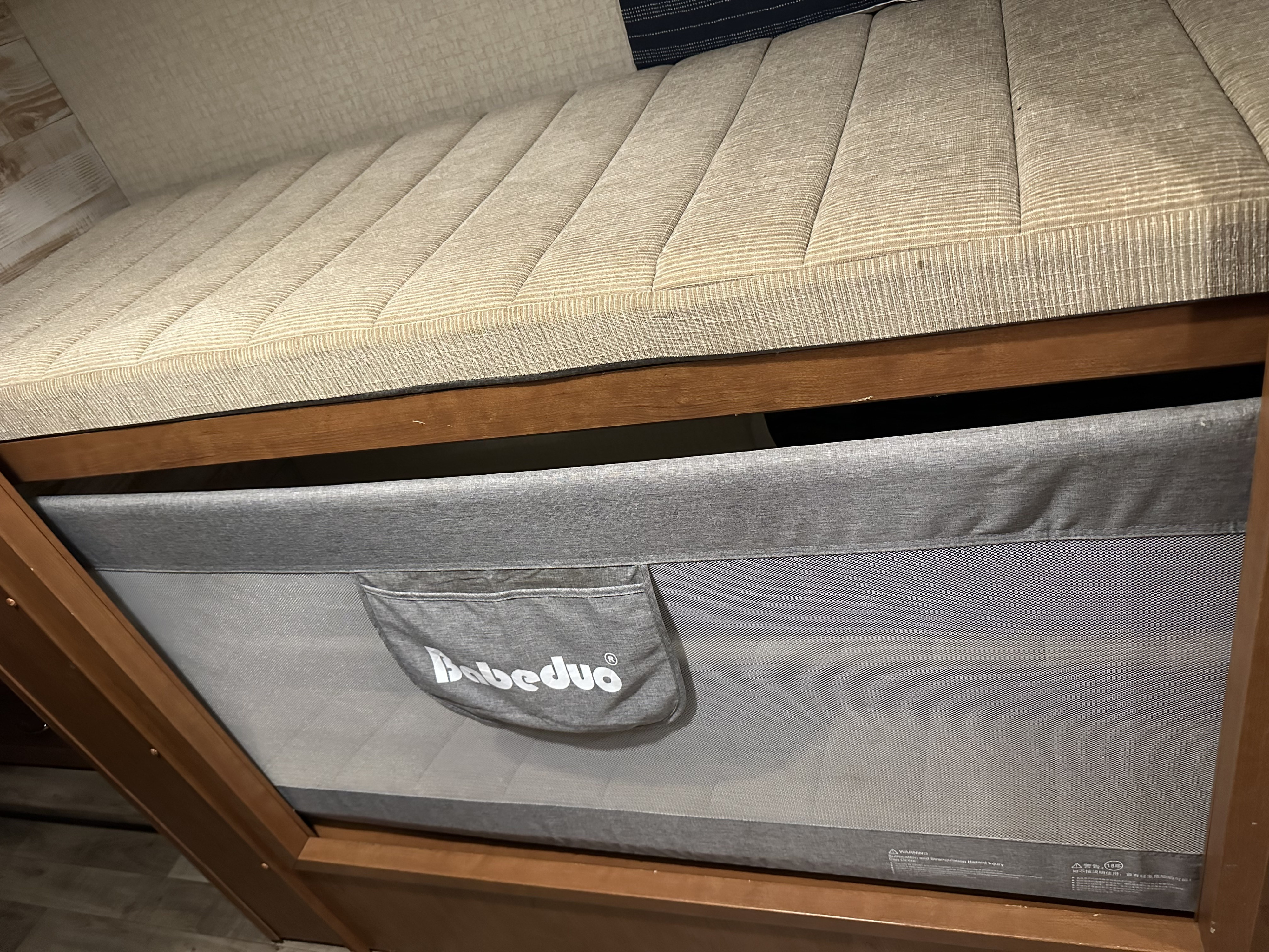 RV rental interior showing a Bebedúo baby playard neatly tucked under a beige bed, ideal for family travel.. Winnebago Minnie Winnie 2018