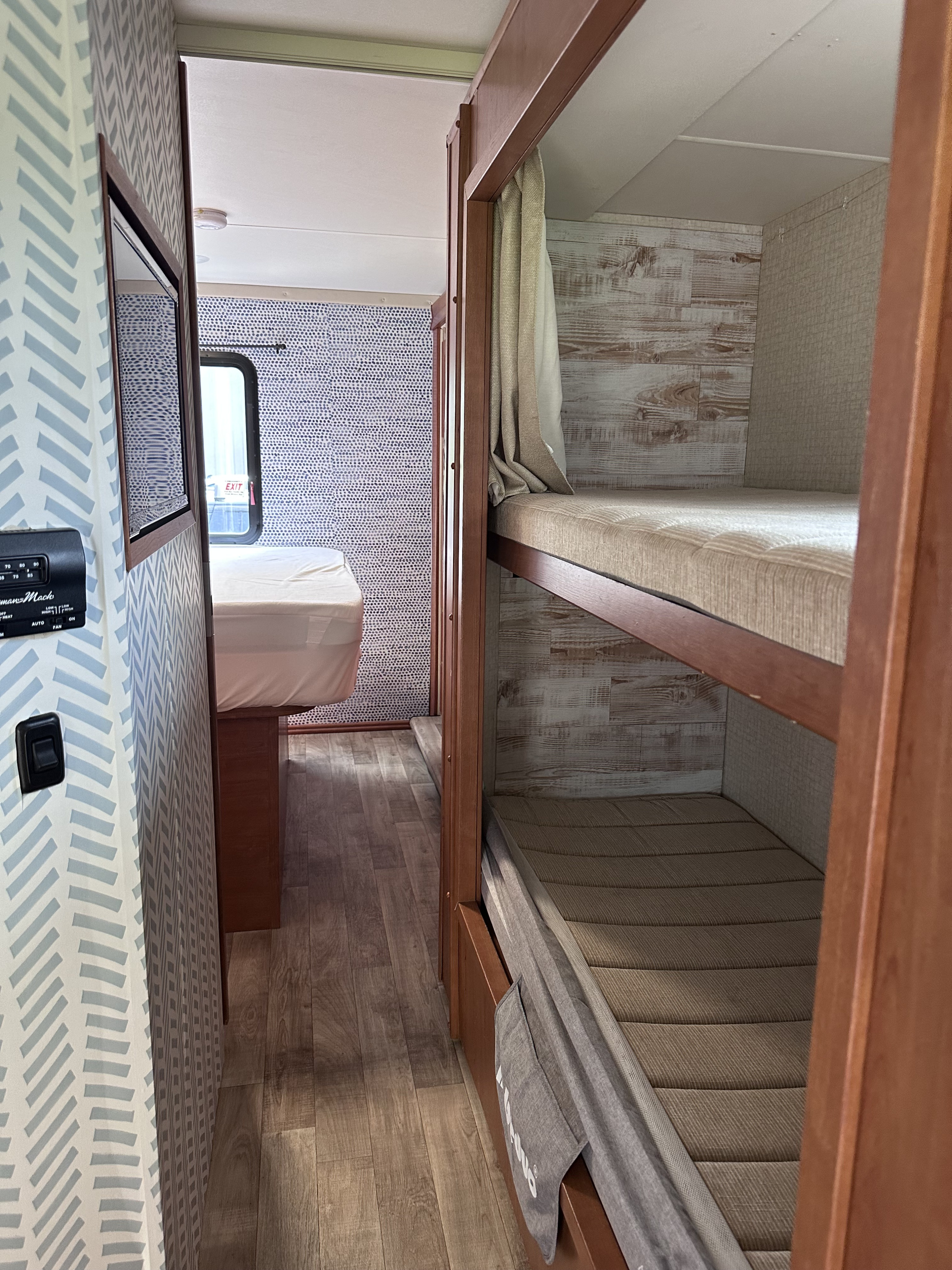 Modern RV rental interior with a main bed, bunk beds, and patterned walls. Wood-look flooring is visible.. Winnebago Minnie Winnie 2018