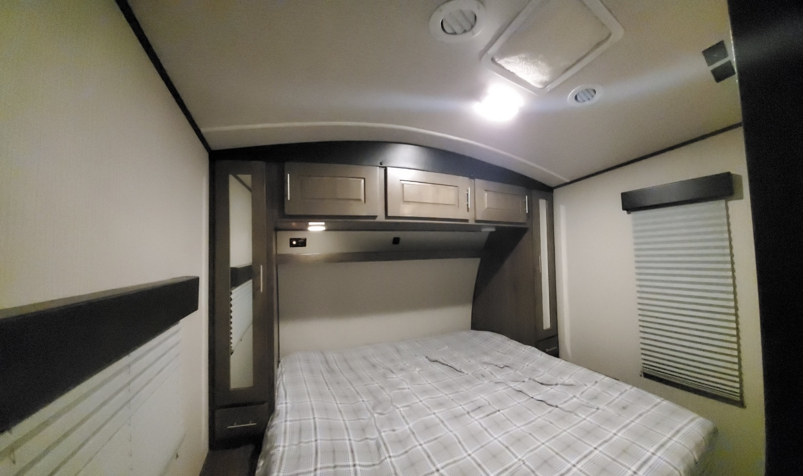 Inside an RV rental: cozy bedroom featuring a plaid bed, ample overhead storage, and side wardrobes with mirrors.. Other Other 2019