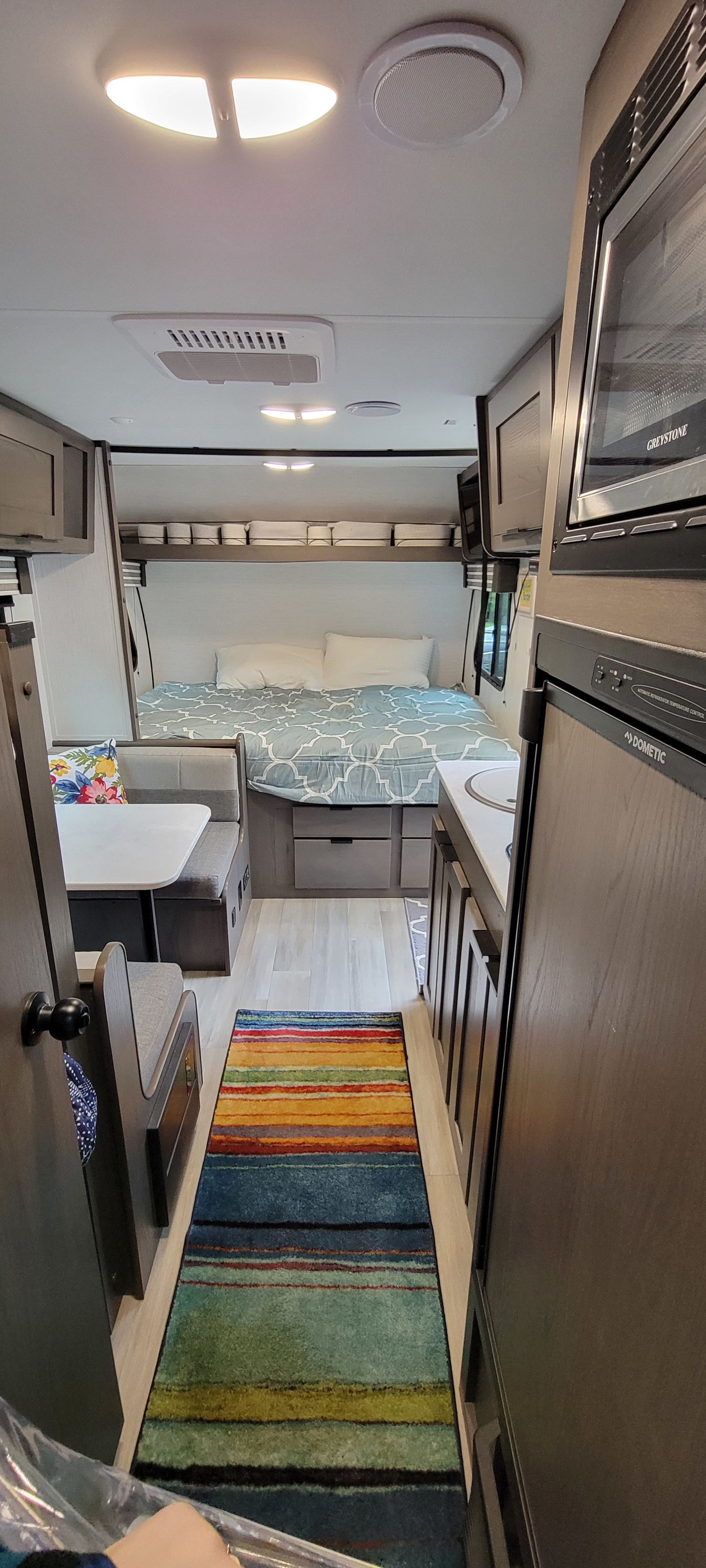 Cozy RV rental interior featuring a compact bedroom, dining area, kitchen with appliances, and a vibrant striped rug.. Heartland RVs Mallard 2022
