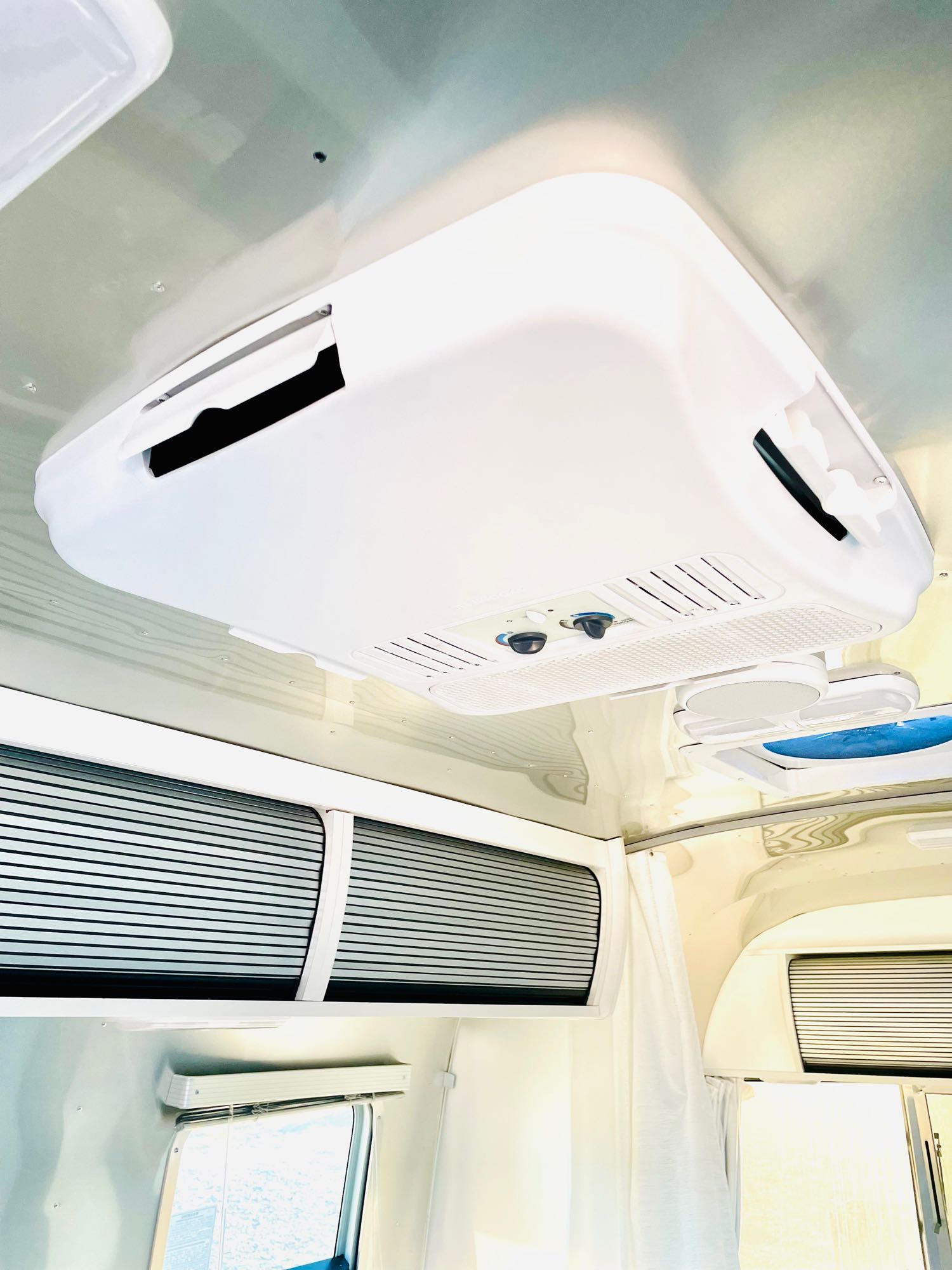 Modern RV rental interior with a prominent white ceiling AC unit, fan, and overhead slatted storage.. Airstream Bambi 2023