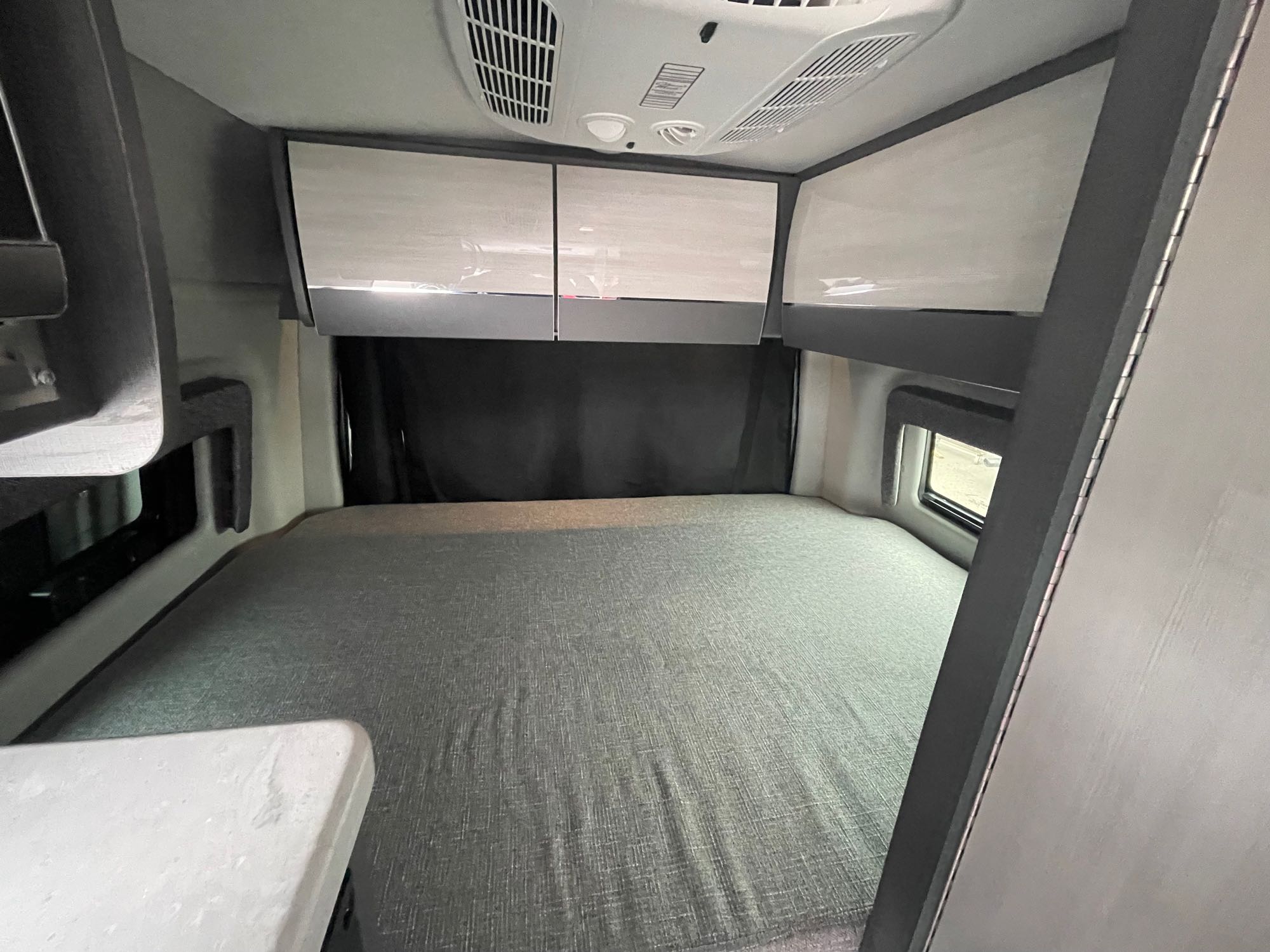 Spacious RV rental bedroom with a large gray bed, overhead cabinets, and AC unit for a comfortable journey.. THOR MOTOR COACH Tranquility 2024