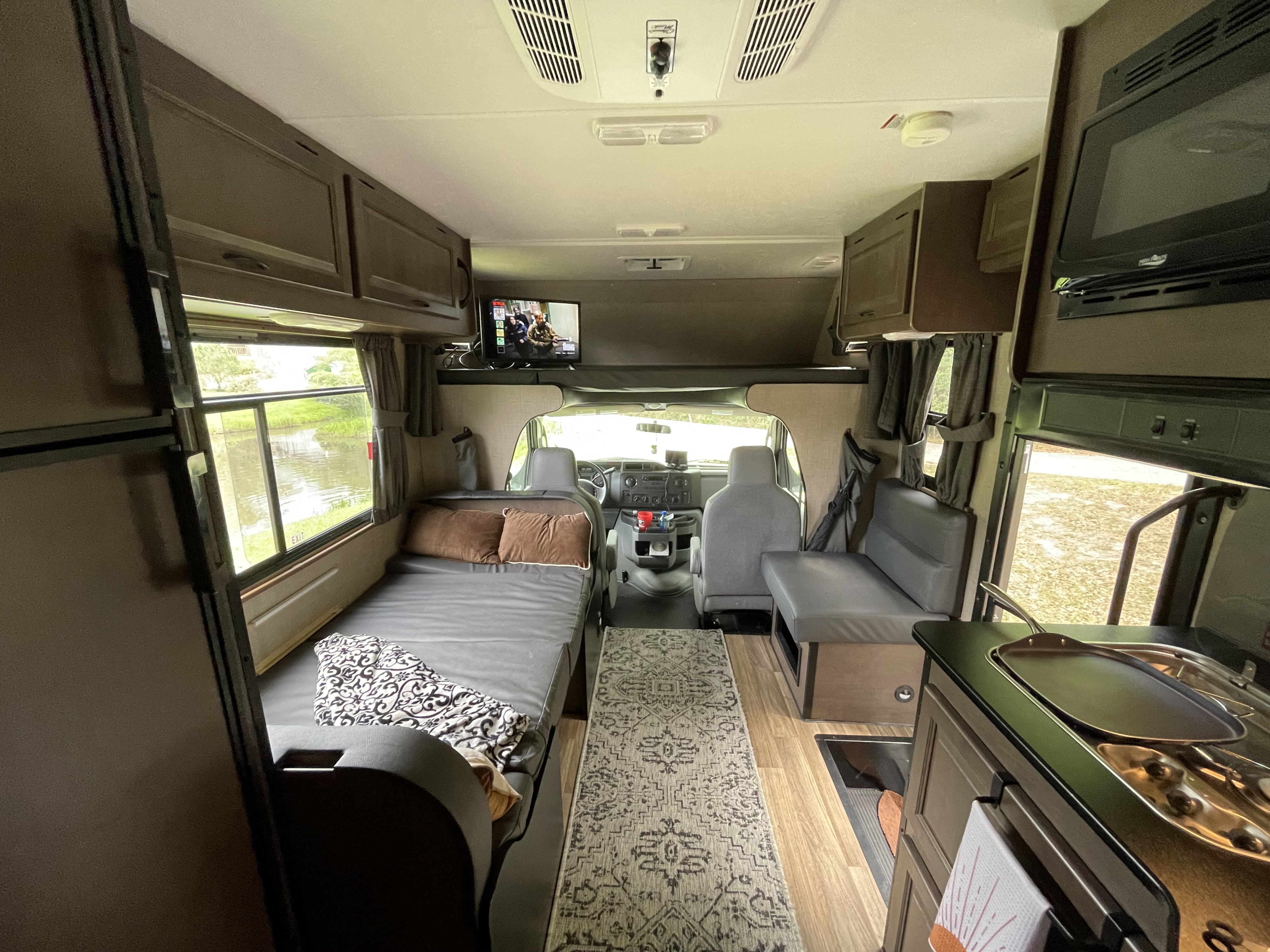 Inside a comfy rv rental, showing the interior with a bed, kitchen, driver's cab, and window view of water.. Wayfarer Wayfarer Motorhome 2020