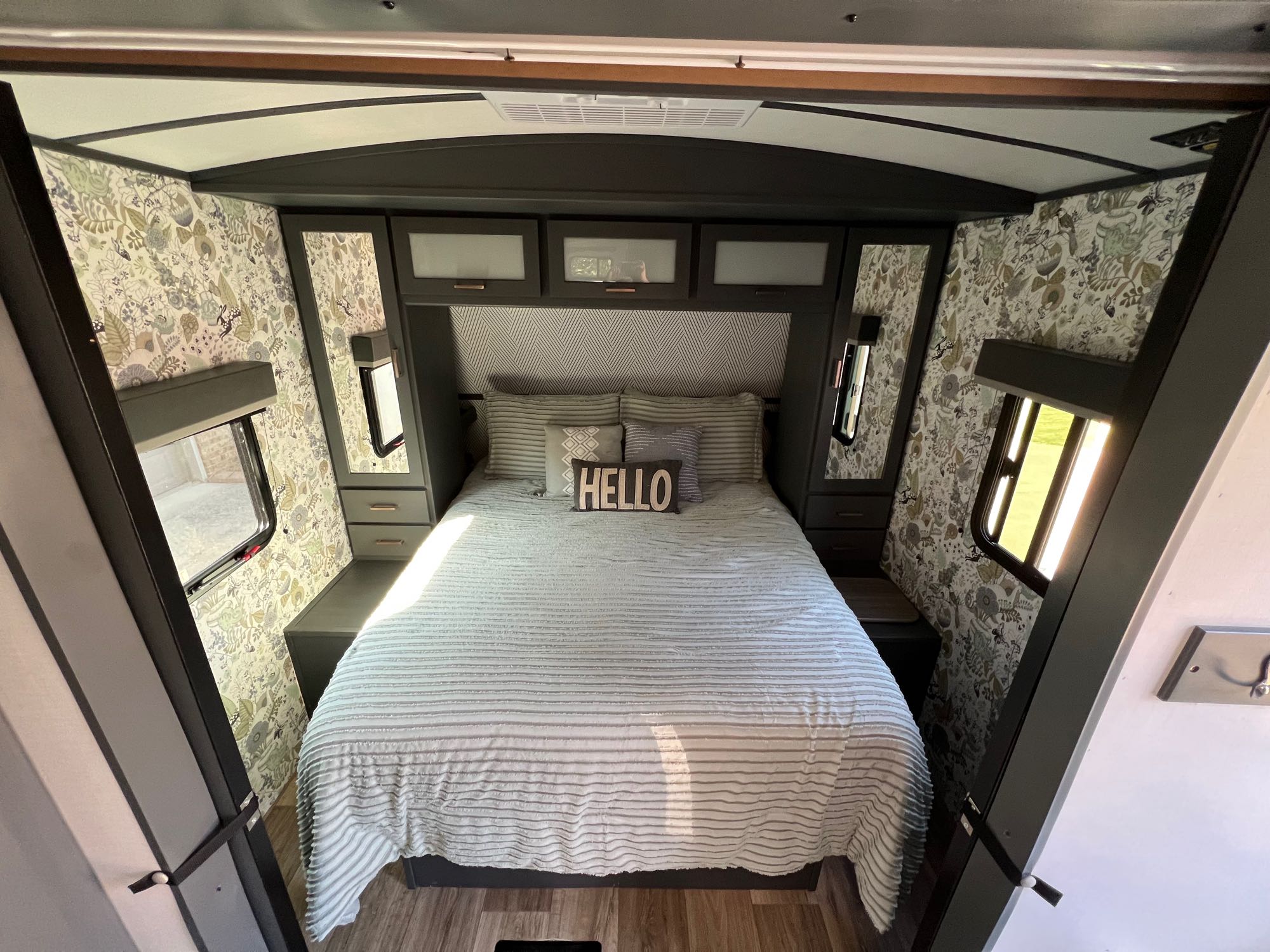 Cozy RV rental bedroom featuring dark cabinetry, botanical wallpaper, and a comfortable striped bed.. Keystone RV Bullet Ultra Lite 2022
