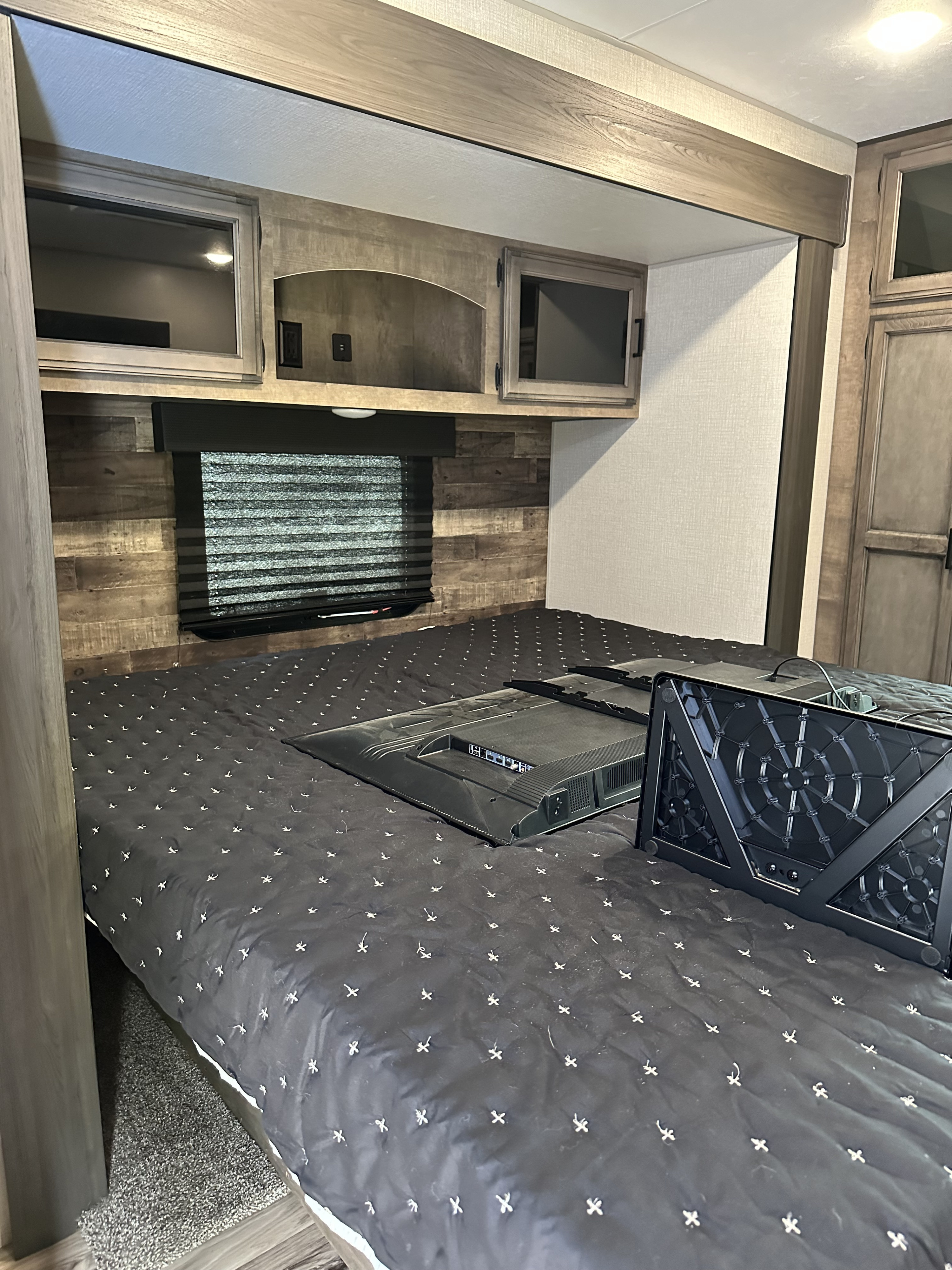 Inside an RV rental: a compact bedroom with a queen bed, window, overhead storage, and a TV on the bed for travelers.. Sport Trek Touring 2021