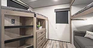 This RV rental bunkhouse shows a light-filled interior with two bunk beds, a central storage unit, and a small sofa.. Grand Design Reflection 2023