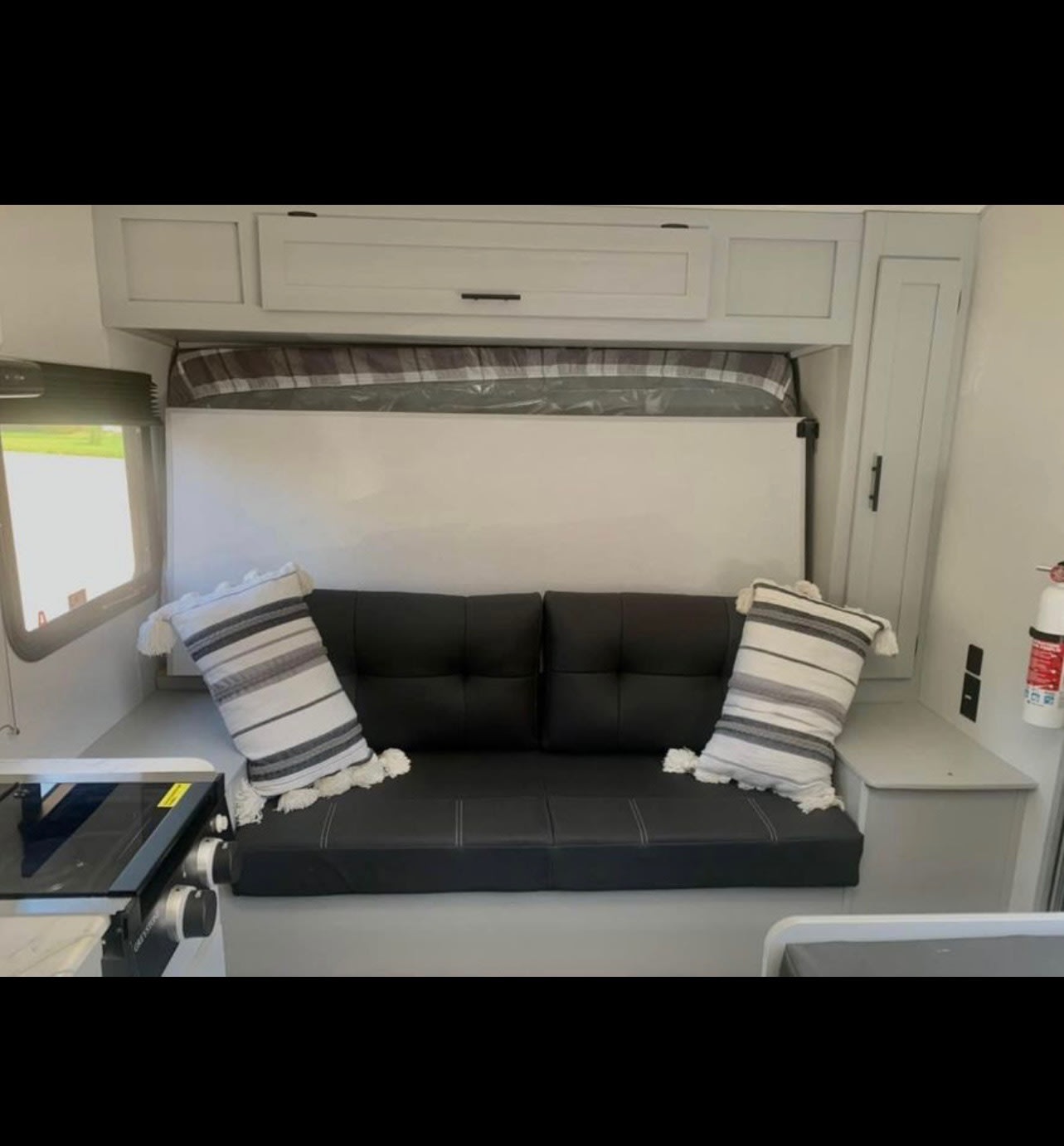 RV rental interior: a black sofa converts to a bed under white cabinets. Features a compact kitchen & window.. Forest River Salem FSX PLATINUM 2021
