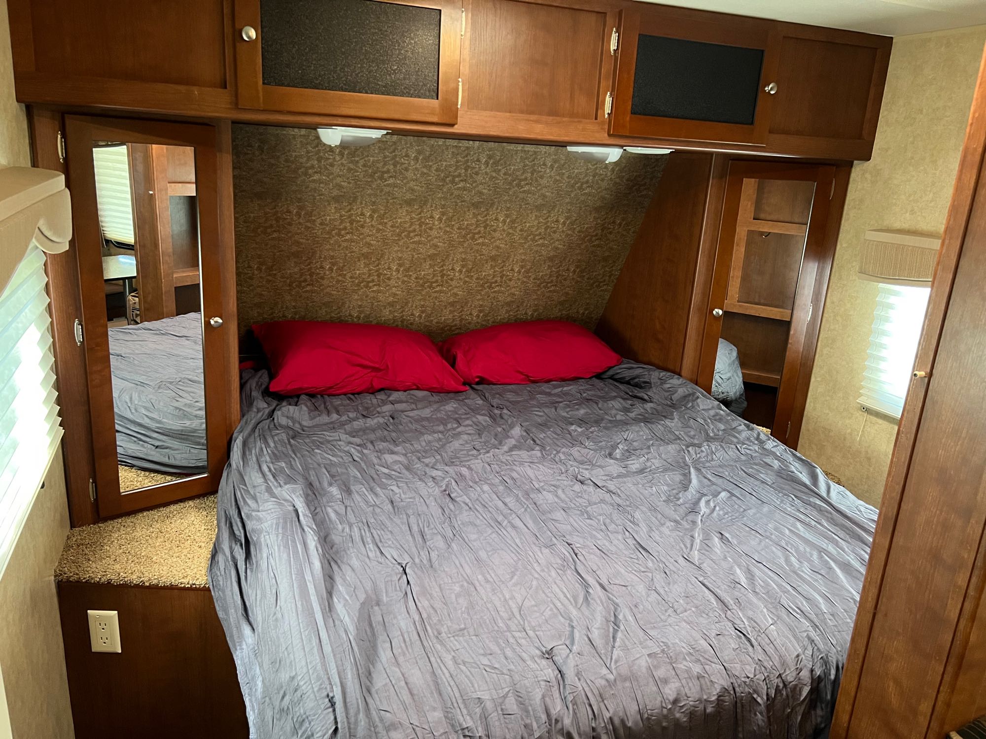 Inside a cozy RV rental bedroom: grey bed, red pillows, wood cabinets & mirrored doors. A compact, inviting space.. Dutchmen Kodiak 2012