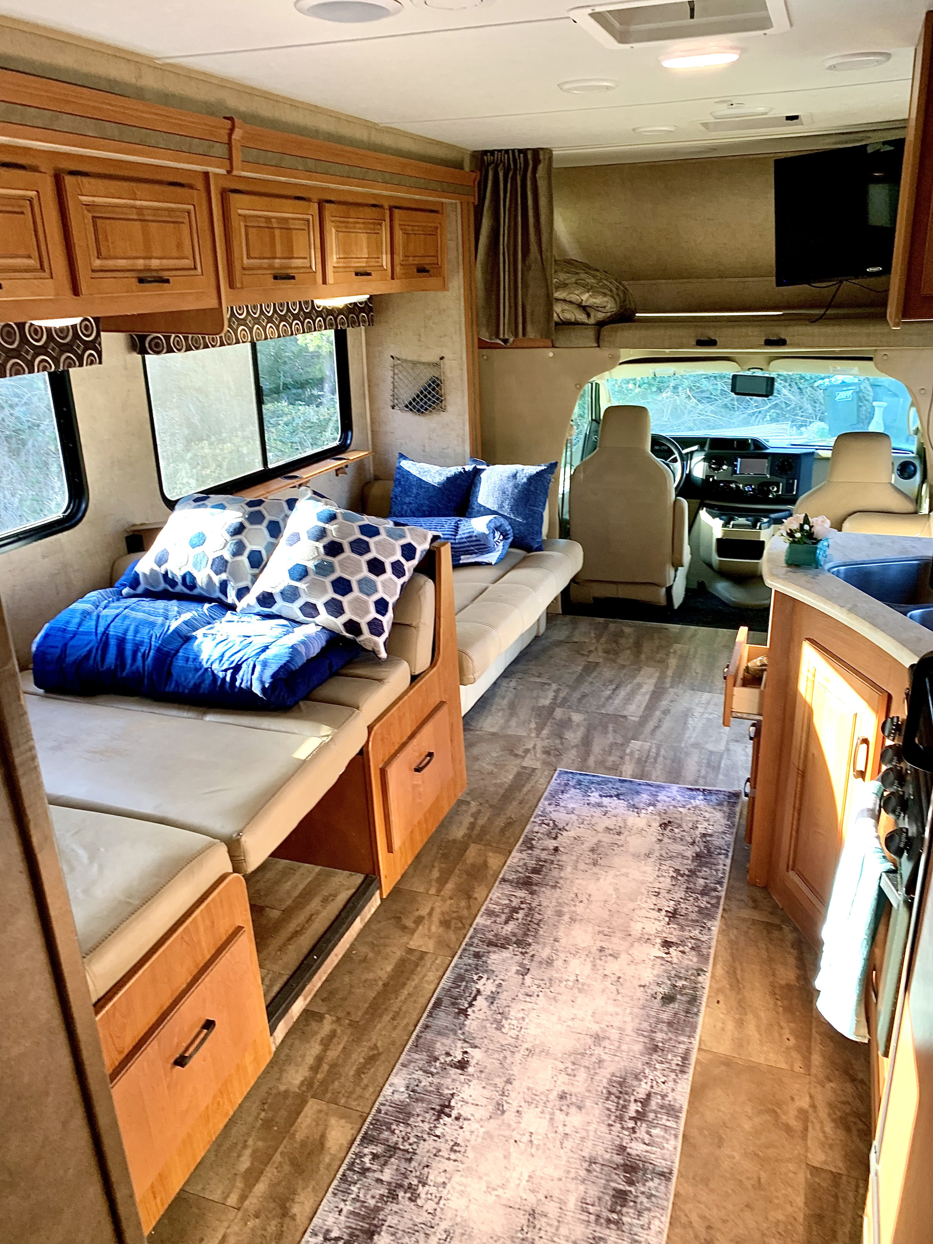 Spacious RV rental interior featuring a bed/dinette, sofa seating, kitchen, and overhead wood cabinets.. Forest River Sunseeker 2016