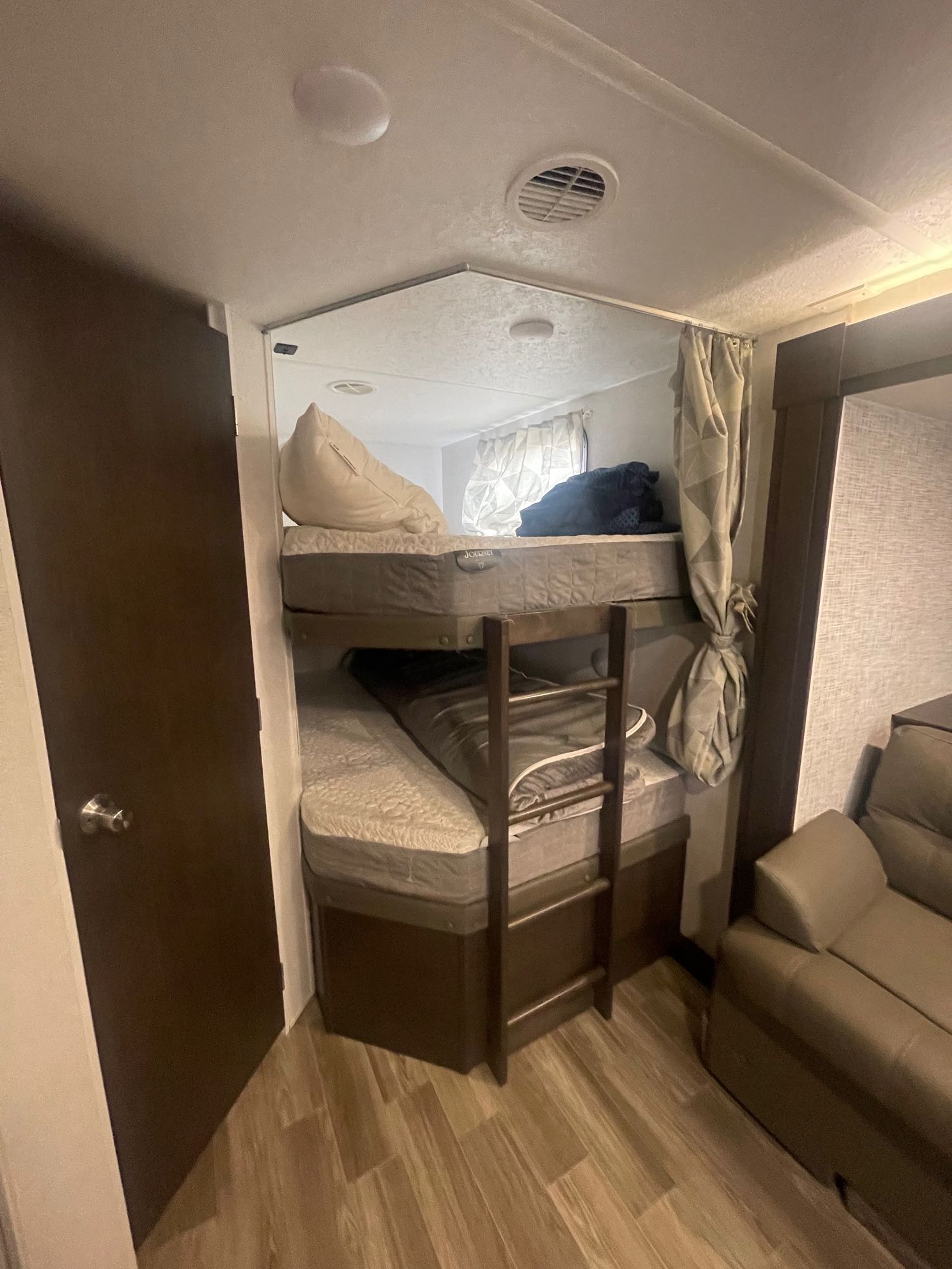 Cozy RV rental interior featuring two-tier bunk beds with a ladder, and a comfortable brown sofa on wood laminate flooring.. Forest River Cruise Lite 2019