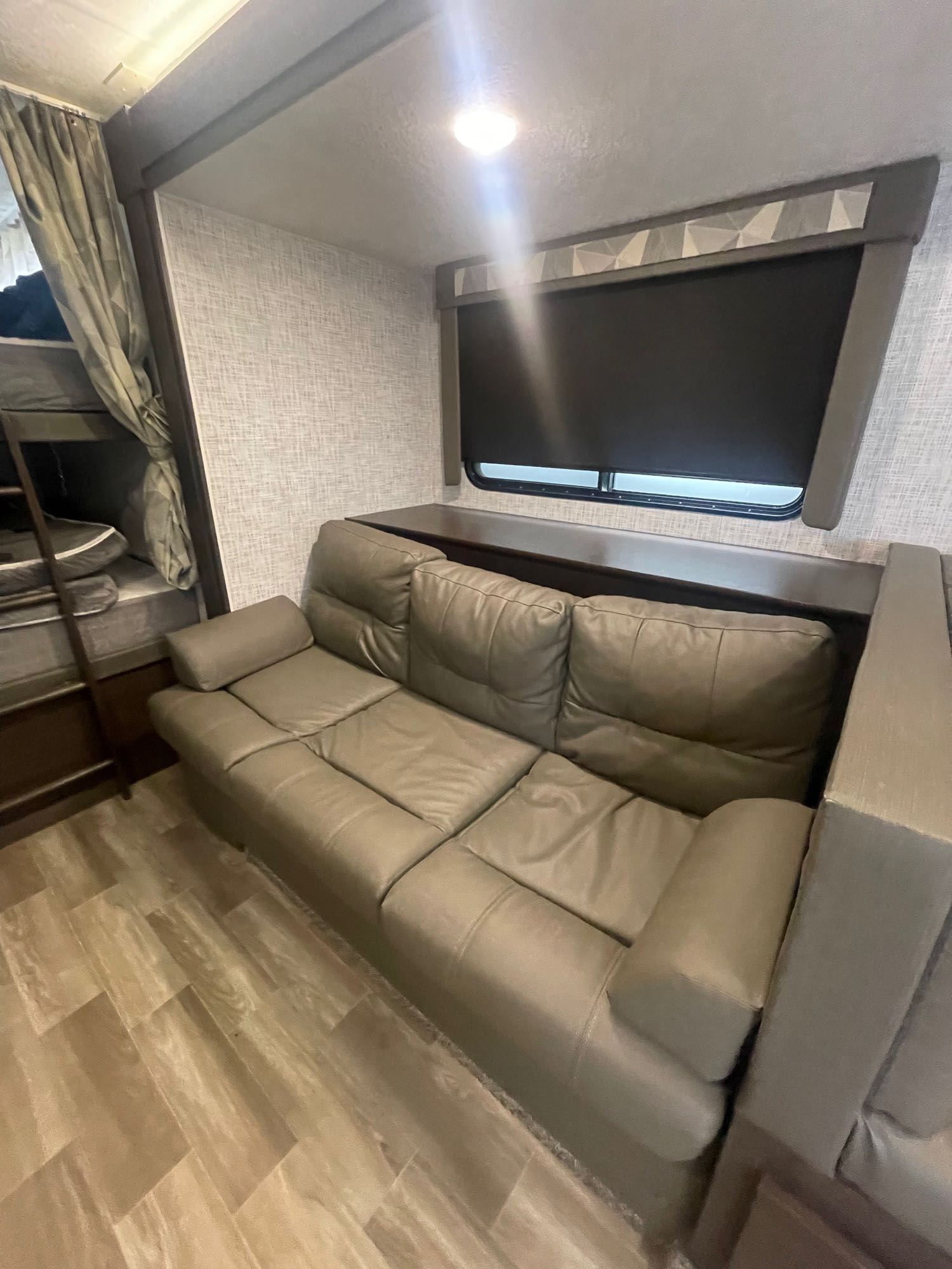 RV rental's interior: comfy gray sofa, bunk beds, window with blind, wood-look floor. Ideal for travel adventures.. Forest River Cruise Lite 2019