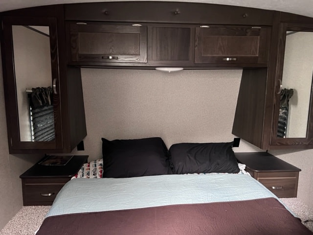 Spacious RV rental bedroom featuring a comfortable bed, mirrored overhead cabinets, and built-in bedside tables.. Keystone RV Springdale 2019