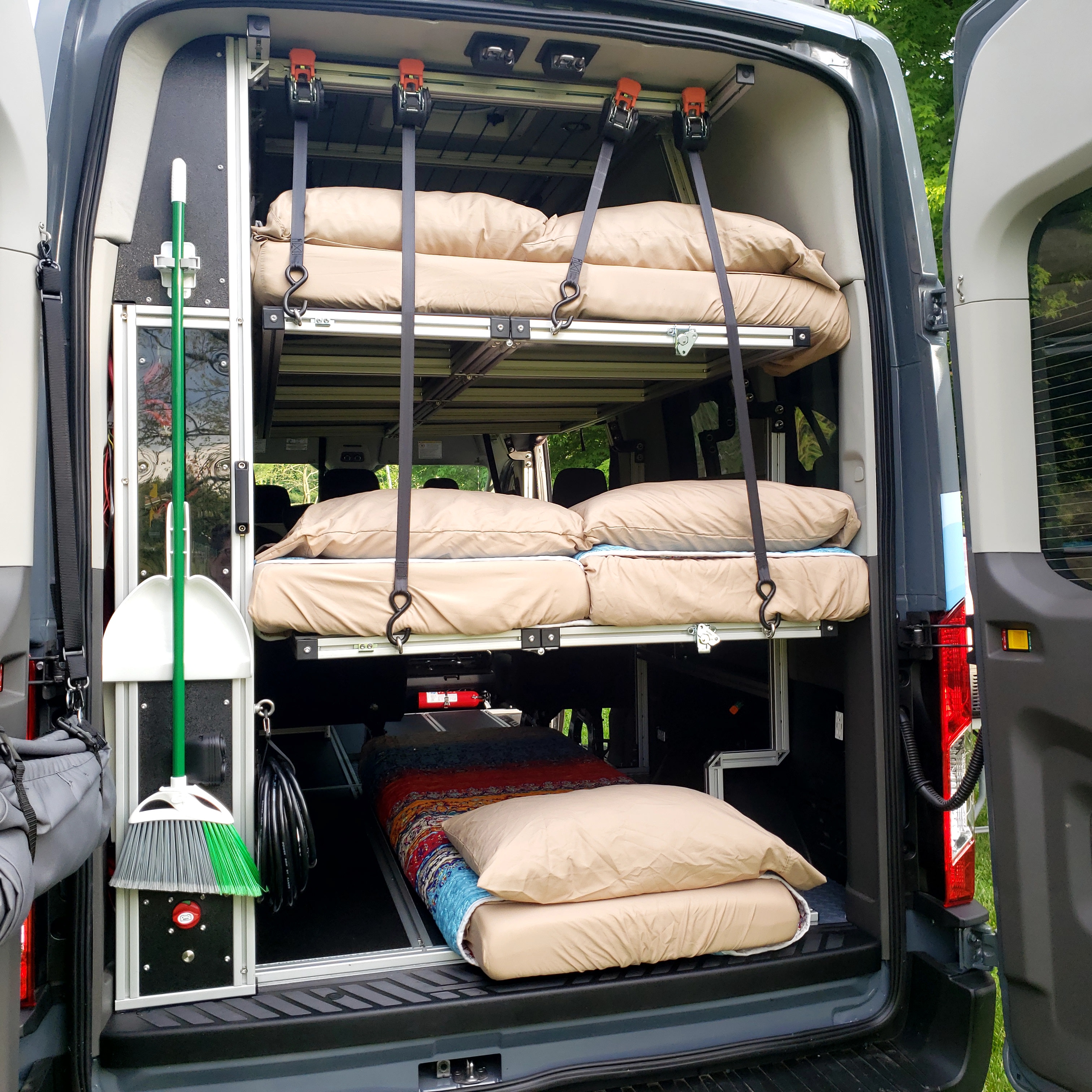 Inside an RV rental van: custom bunk beds for camping, neat storage for a broom & essentials.. Ford Transit 2022