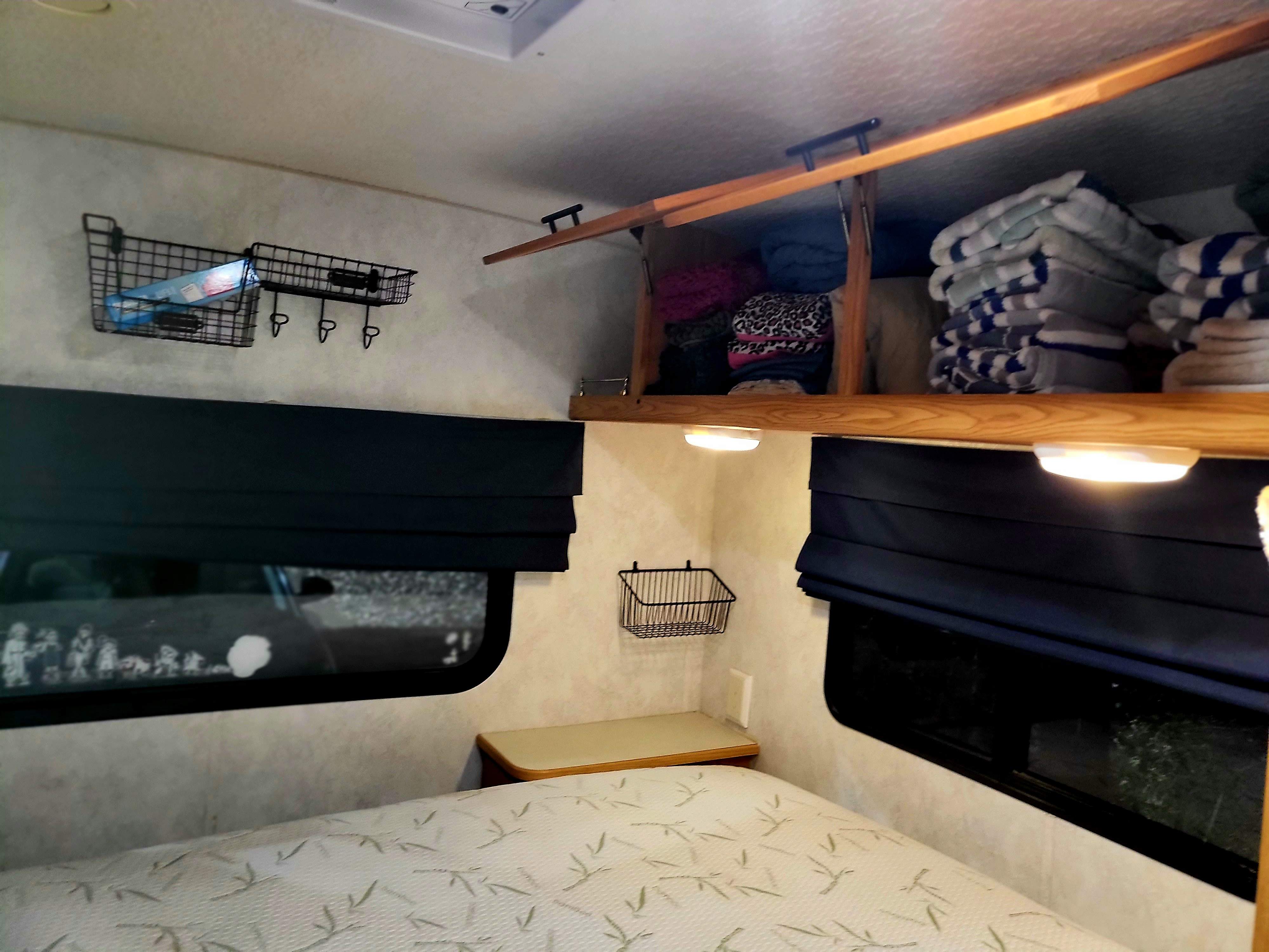 Inside an RV rental: a neat bedroom with a comfy bed, wall-mounted storage baskets, and overhead cabinets for towels & clothes.. Itasca Spirit 2003